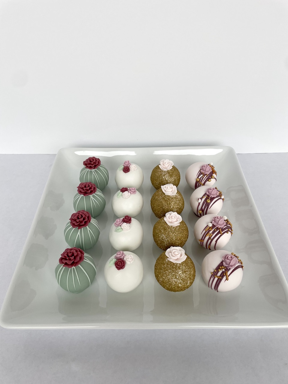 Tray with three rows of decorated spherical desserts, each row with different colors and patterns, on a white surface.