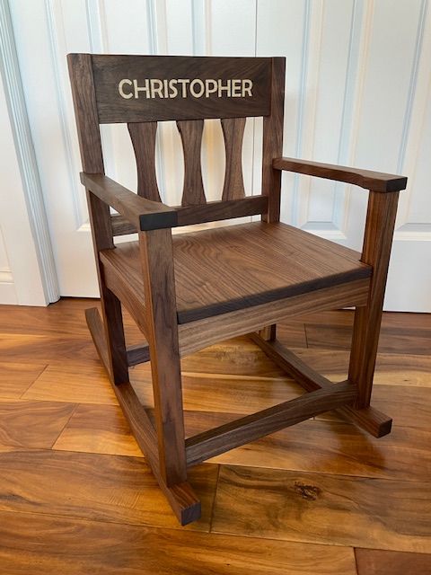 Wooden chair with a sign reading 'CHRISTOPHER' behind it, placed on a hardwood floor, viewed from the side.