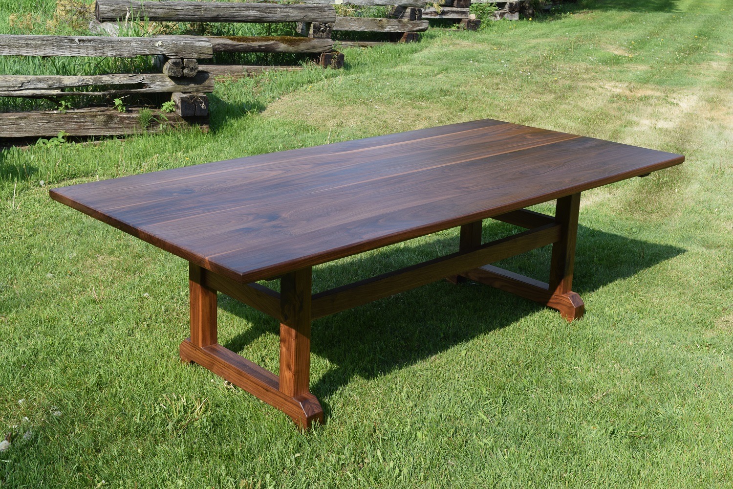 Wooden table outdoors on grass with a wooden fence in background.