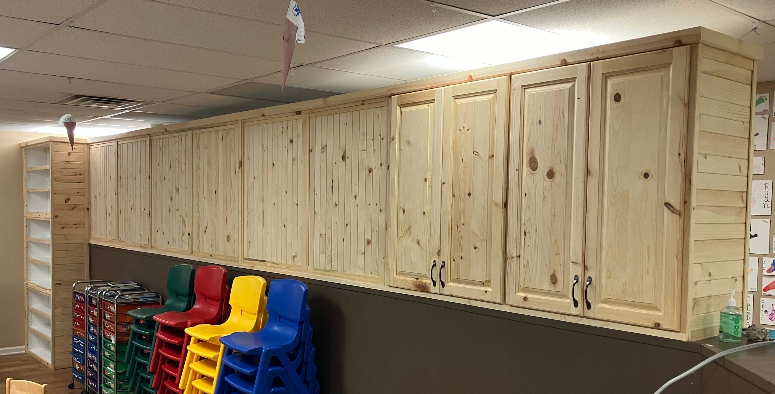 Wooden cabinets mounted on a wall above colorful stacked chairs in a room.