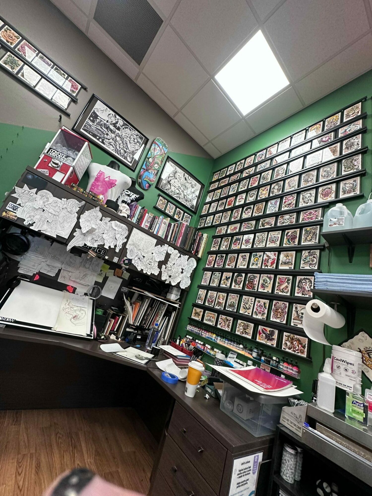 Office with wall of framed photos, desk with papers, books, and office supplies, and a green wall.