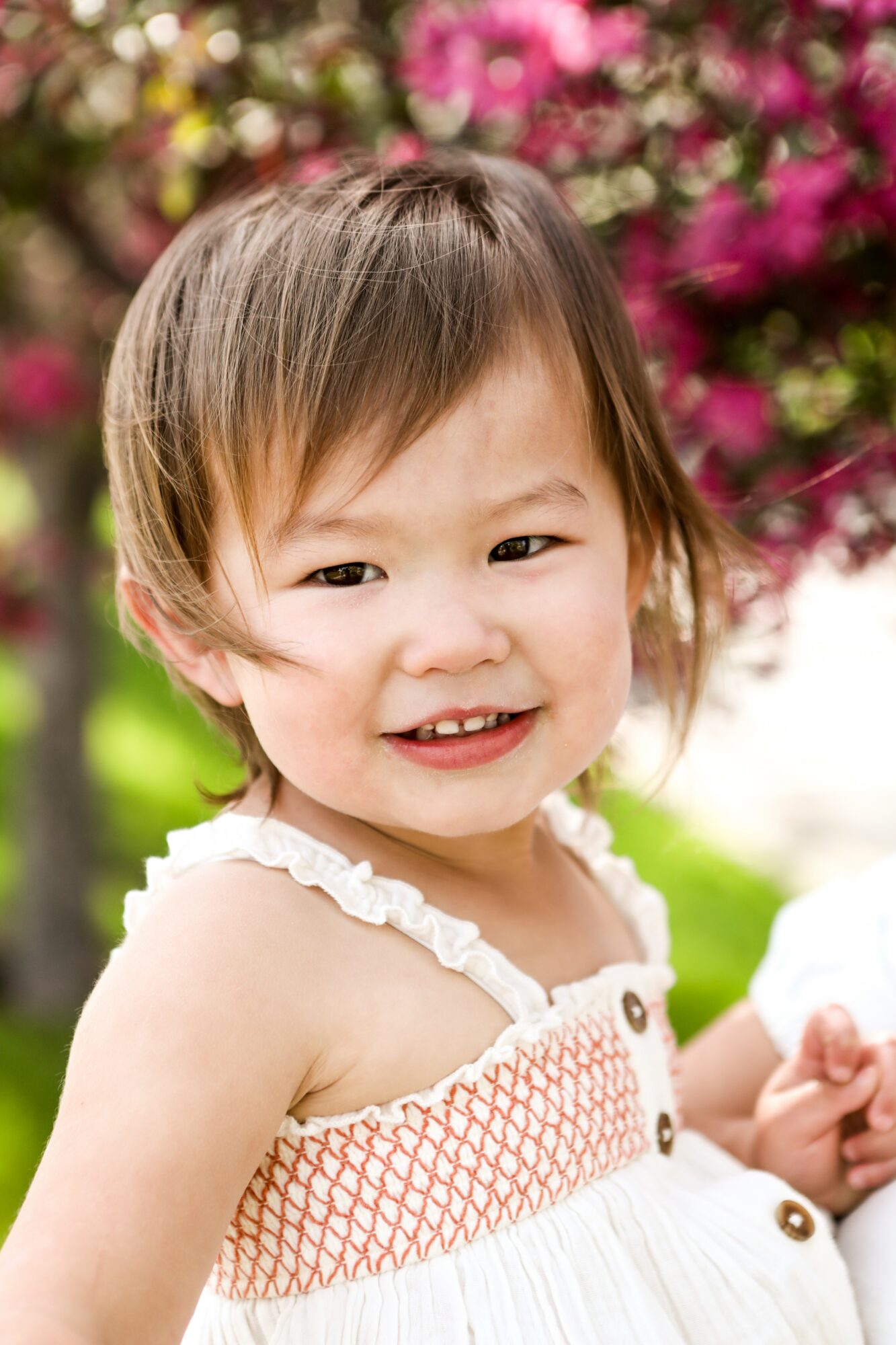 Young girl with short hair smiling outdoors with pink flowers in background