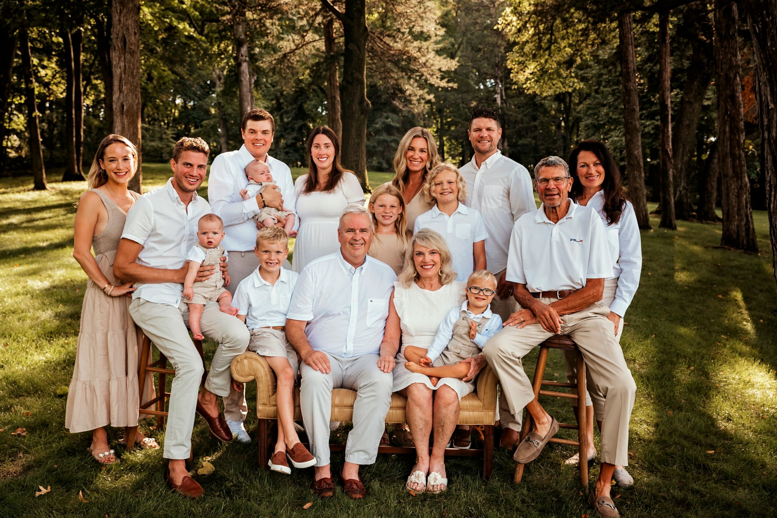 Group of 15 people, including children, posing outdoors in a park with trees and grass, smiling at the camera.