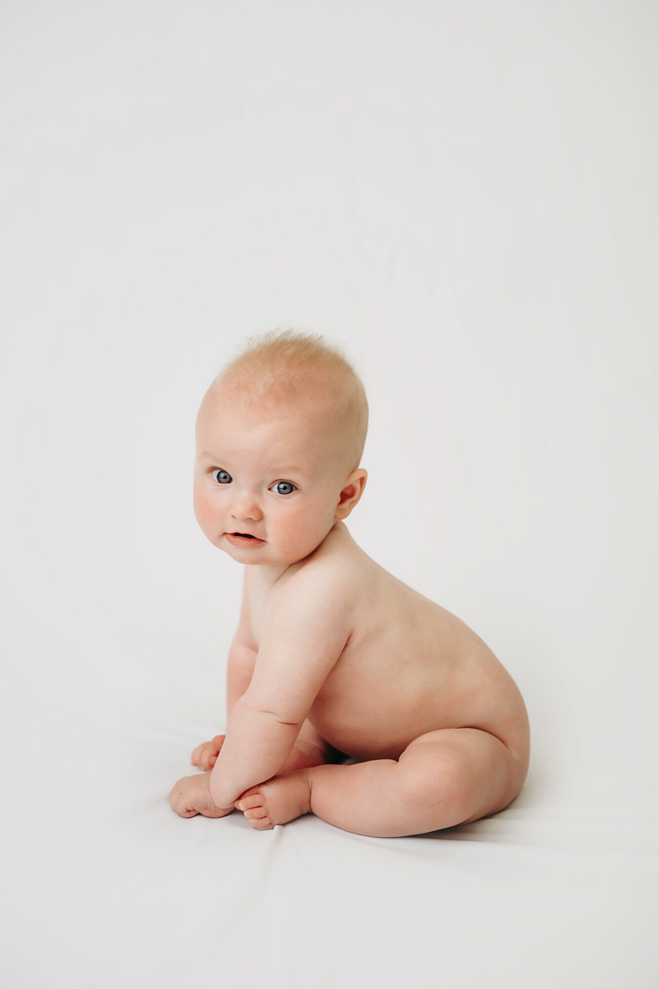 Baby sitting on the floor, looking at the camera, with a plain white background.