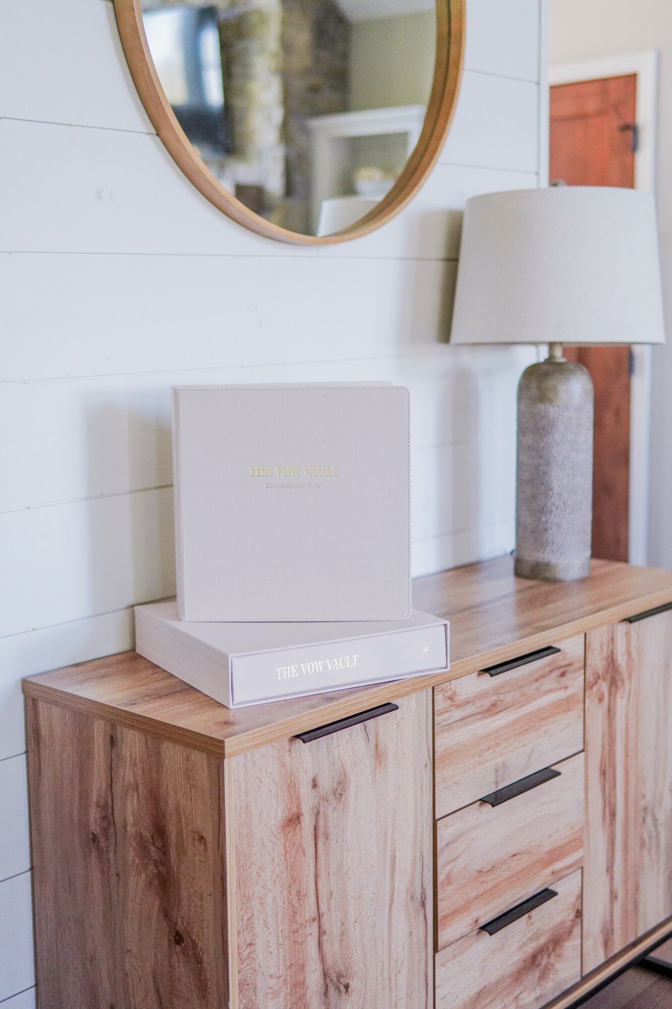 Wooden sideboard with a white speaker and a closed white box on top, a lamp, and a mirror above, in a room.