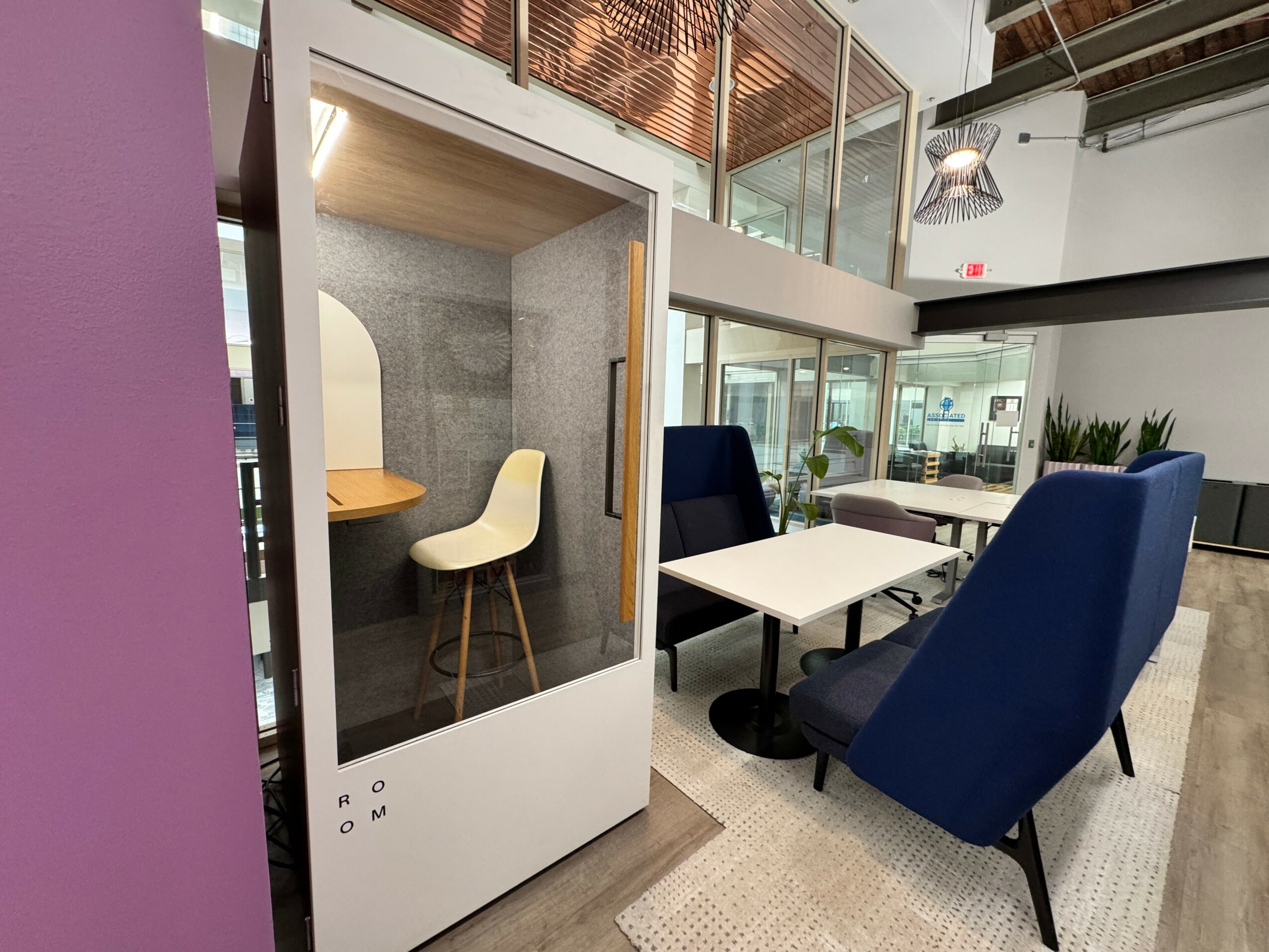 Small enclosed workspace with a round table and two chairs, one white and one beige, inside a modern office.