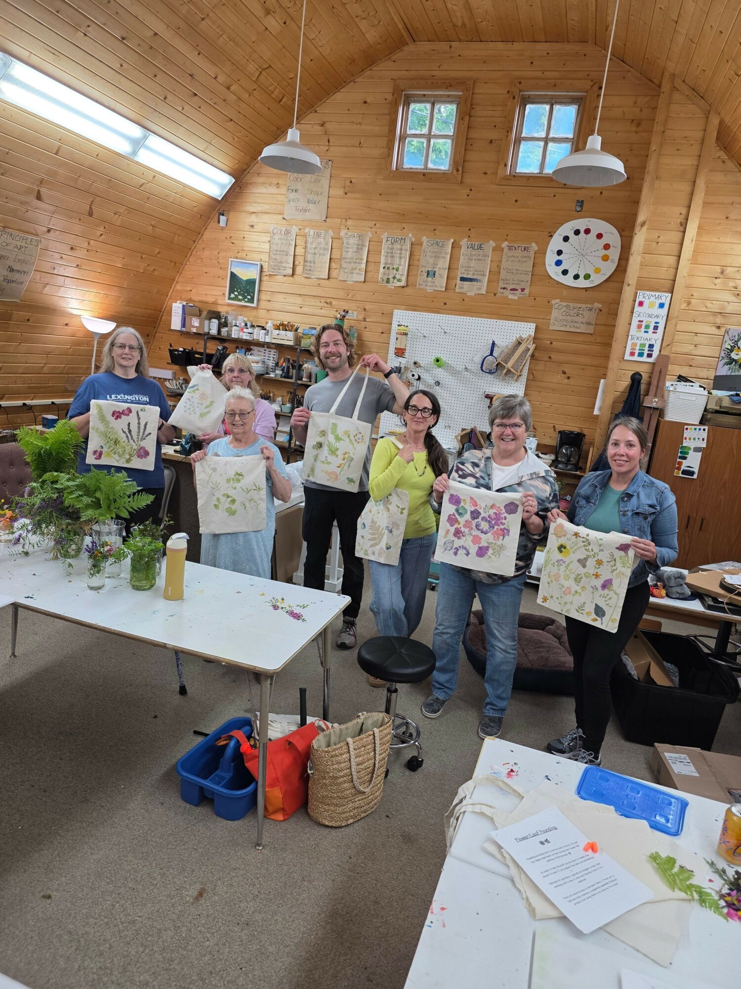 Group of people holding colorful handmade cards in a wooden room with tables and windows.