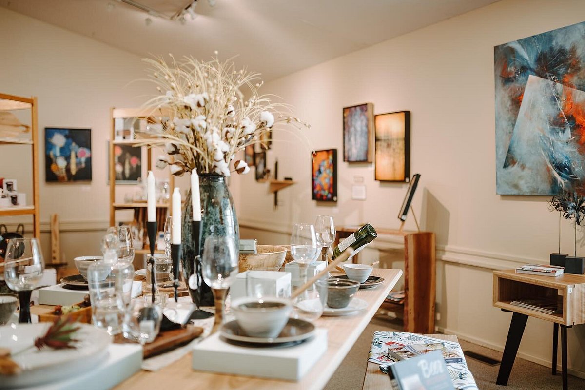 Dining table set with plates, glasses, and a large vase with flowers in an art gallery-style room.