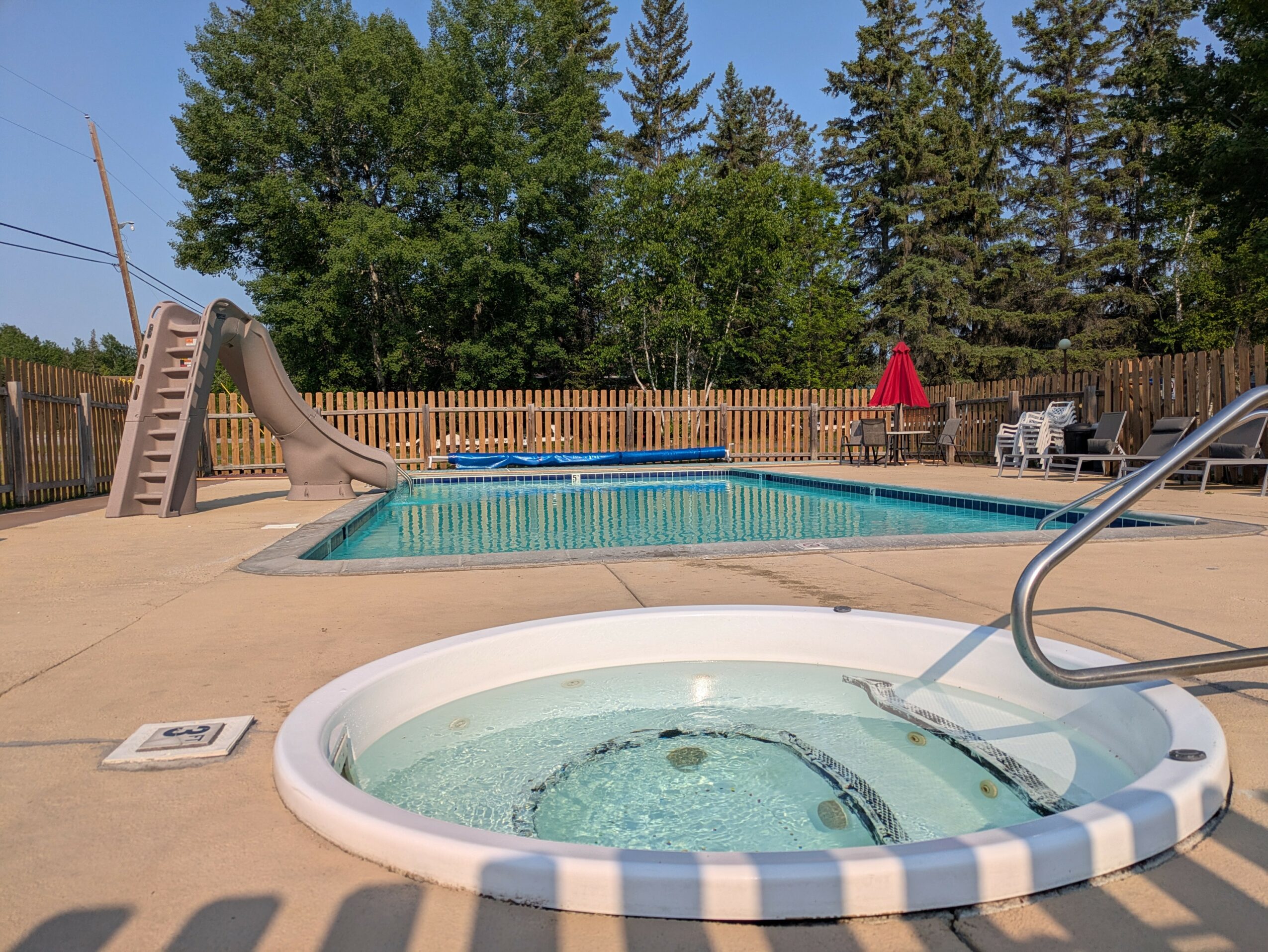 Swimming pool with slide, hot tub, trees, and outdoor furniture in backyard.