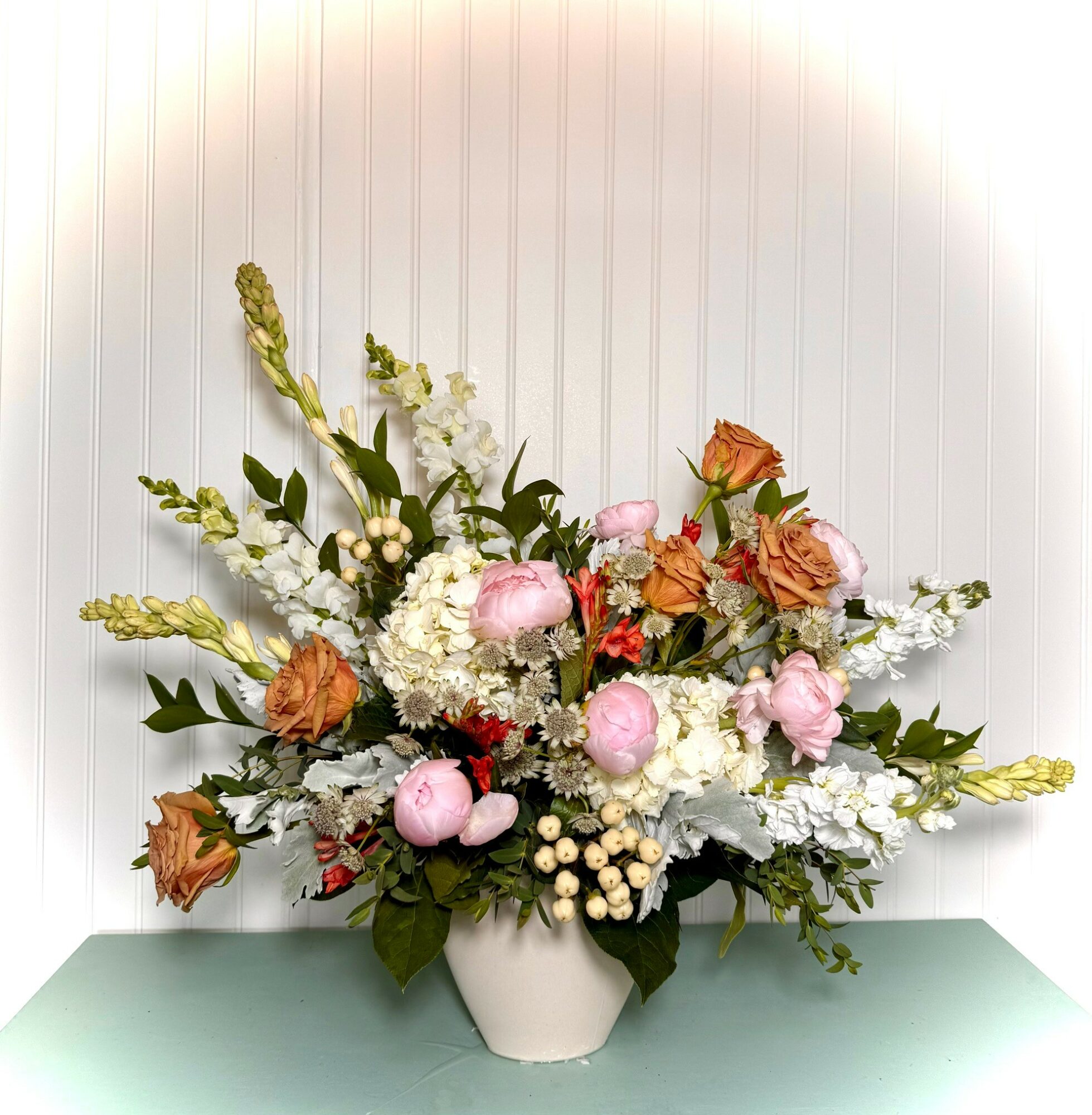 Flower arrangement with pink, orange, and white flowers in a white vase on a green surface, against a white background.