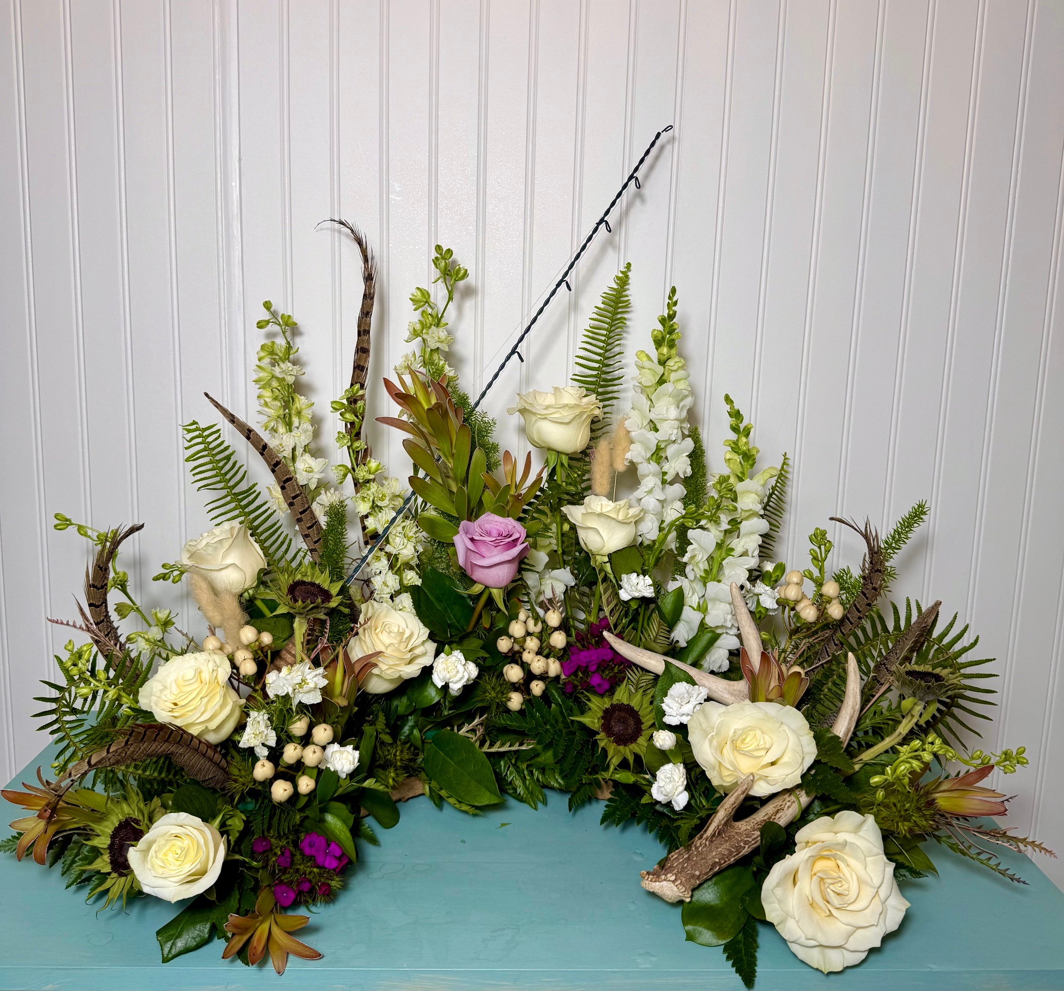 Floral arrangement with white and purple flowers, green foliage, and decorative branches on a light background.