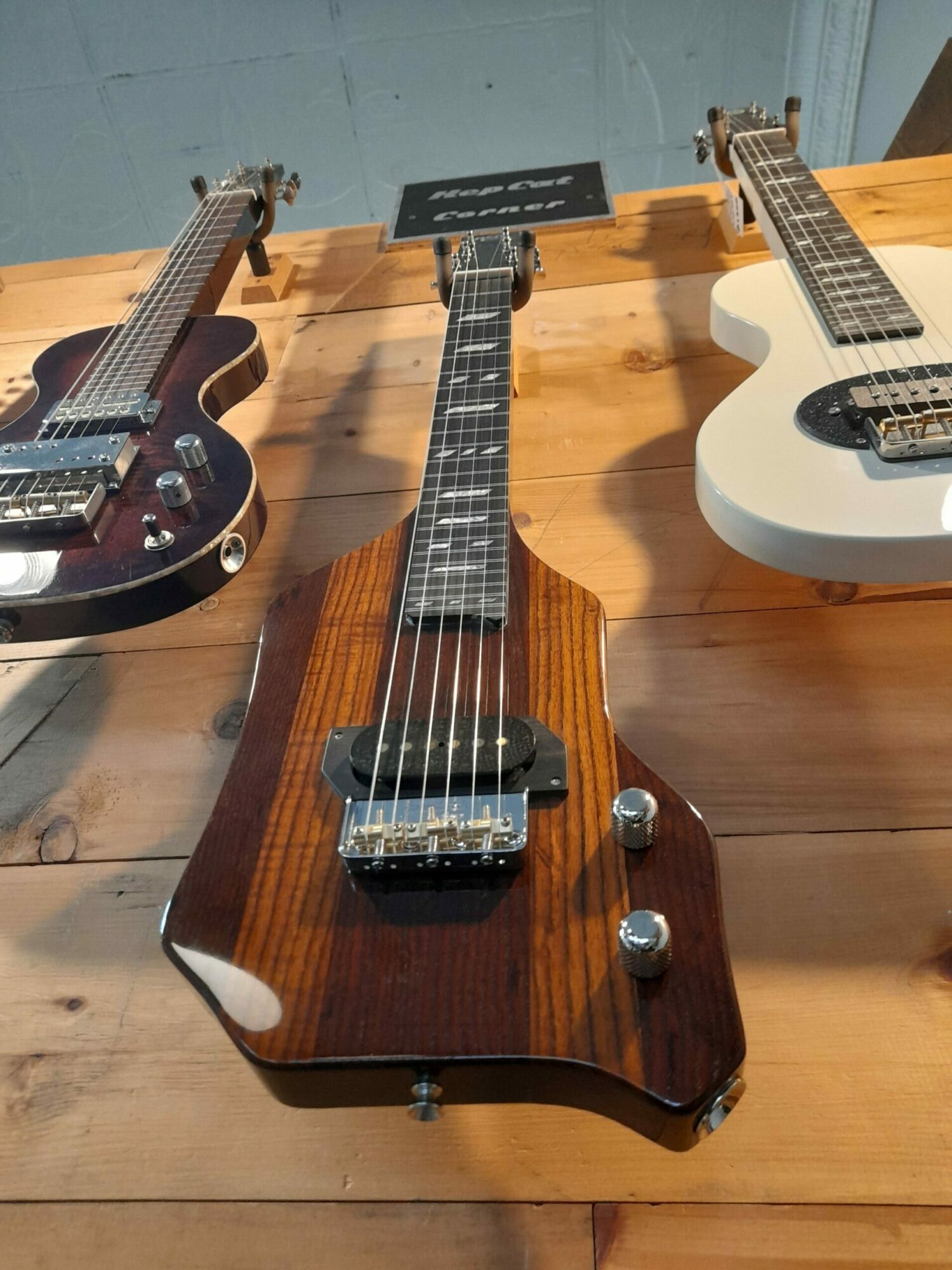 Wooden electric guitar with a dark brown finish, six strings, and control knobs, resting on a wooden surface.