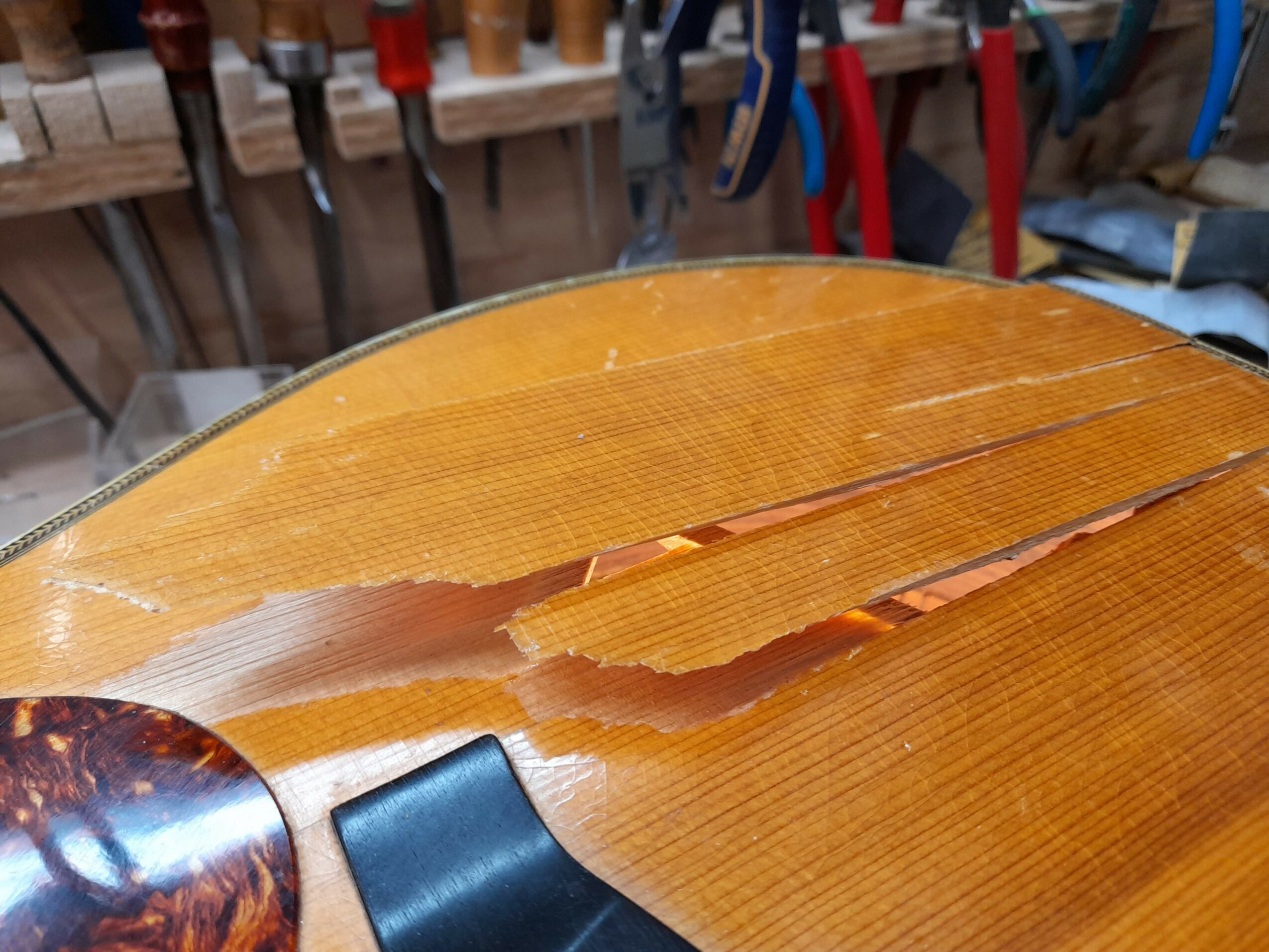 Broken wooden surface with a large crack and splintered edges, in a workshop setting with tools in the background.