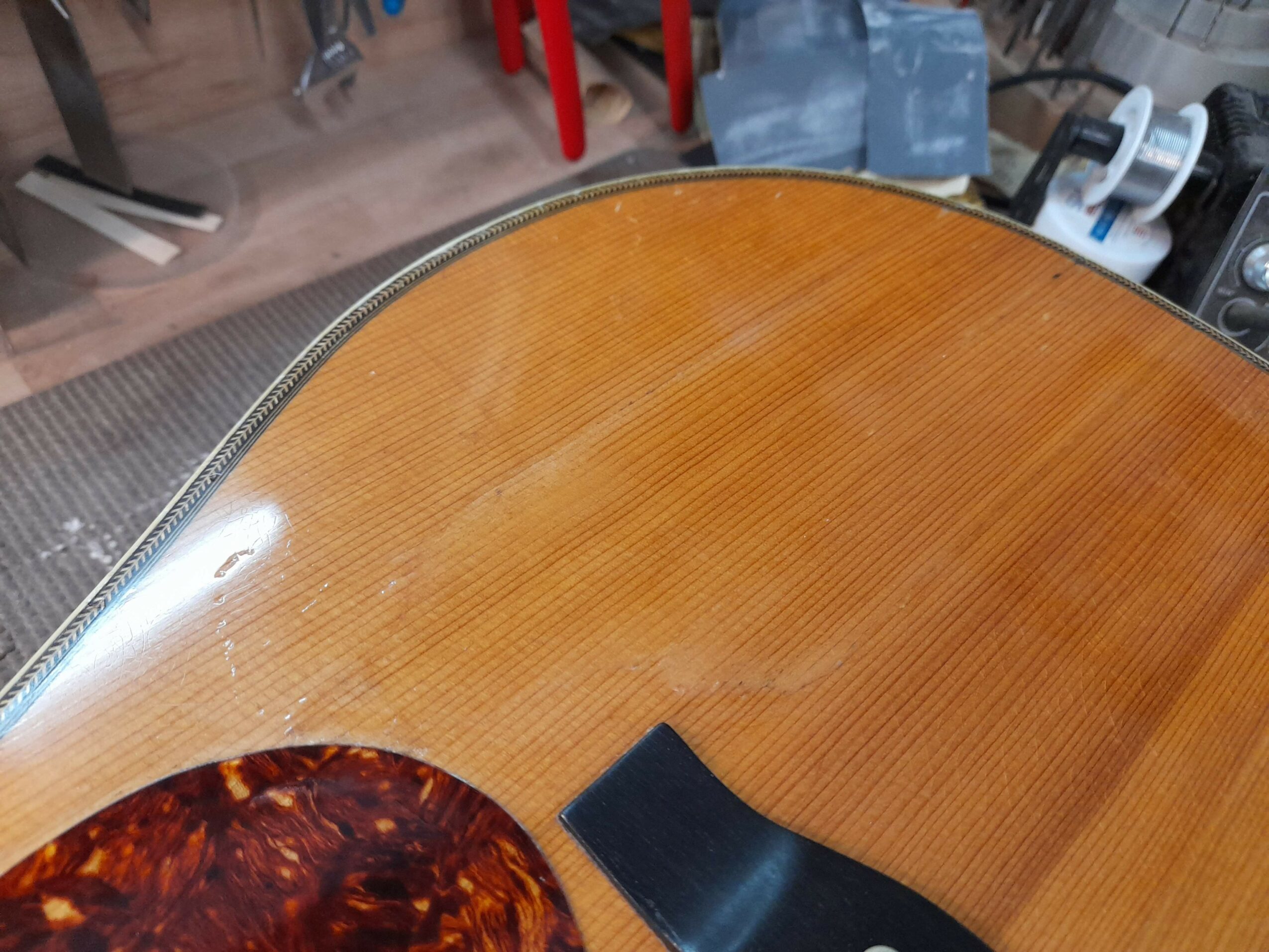 Close-up of a wooden guitar body with a glossy finish, showing the curved edge and part of the top surface.