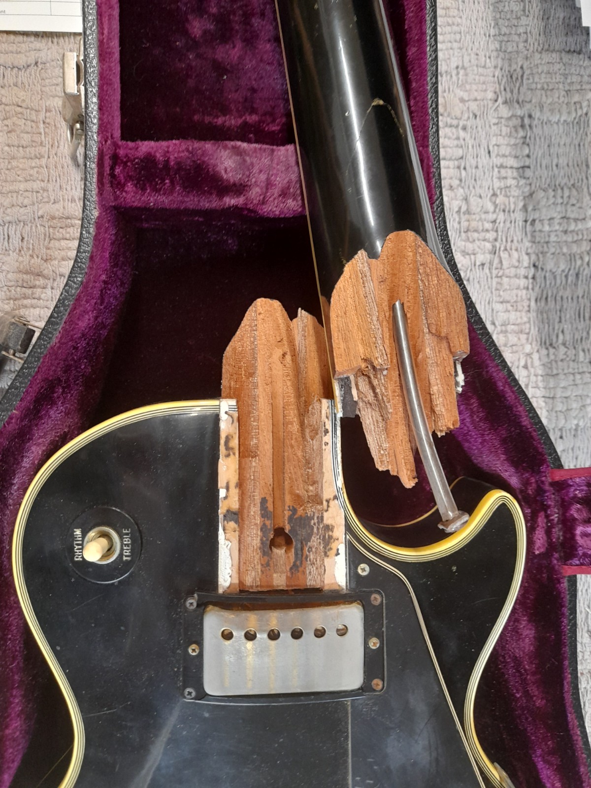 Guitar neck and body inside a purple-lined case, with a wooden block and metal parts visible.