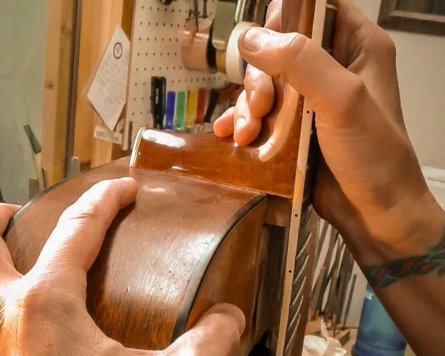 Person shaping wood on a workbench with tools and supplies in background.