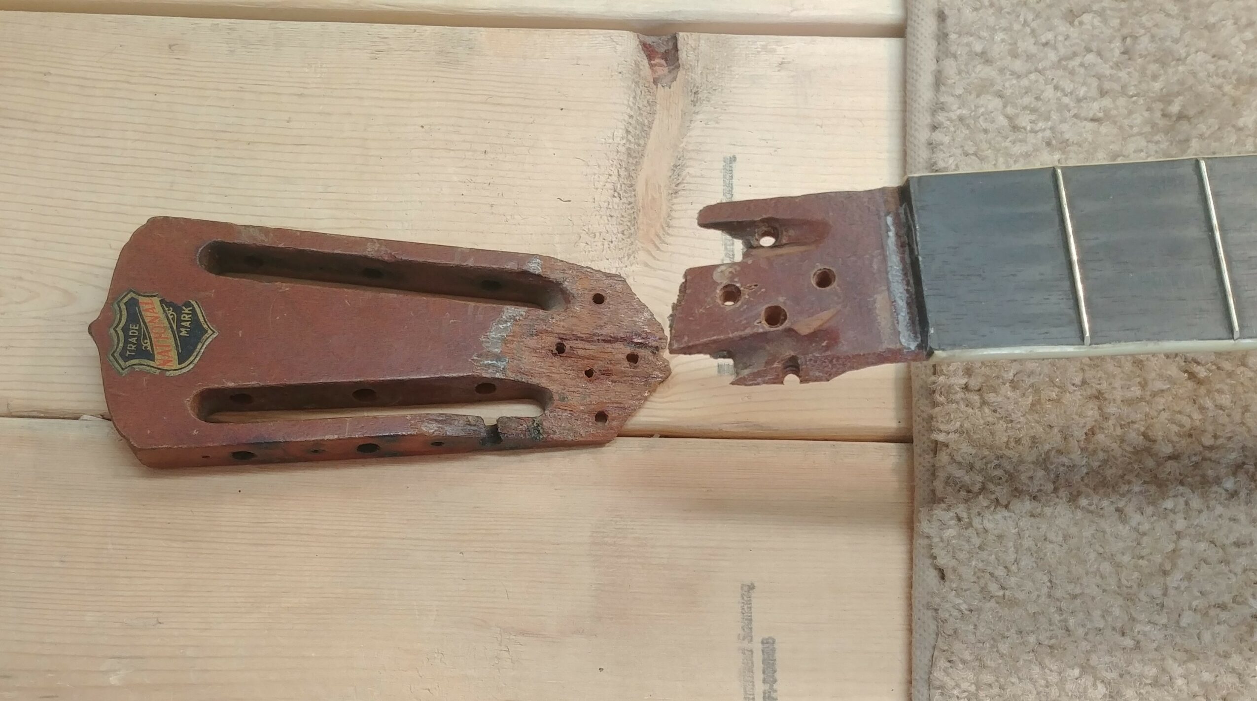 Rusty, broken guitar neck with fretboard attached, lying on a wooden surface.