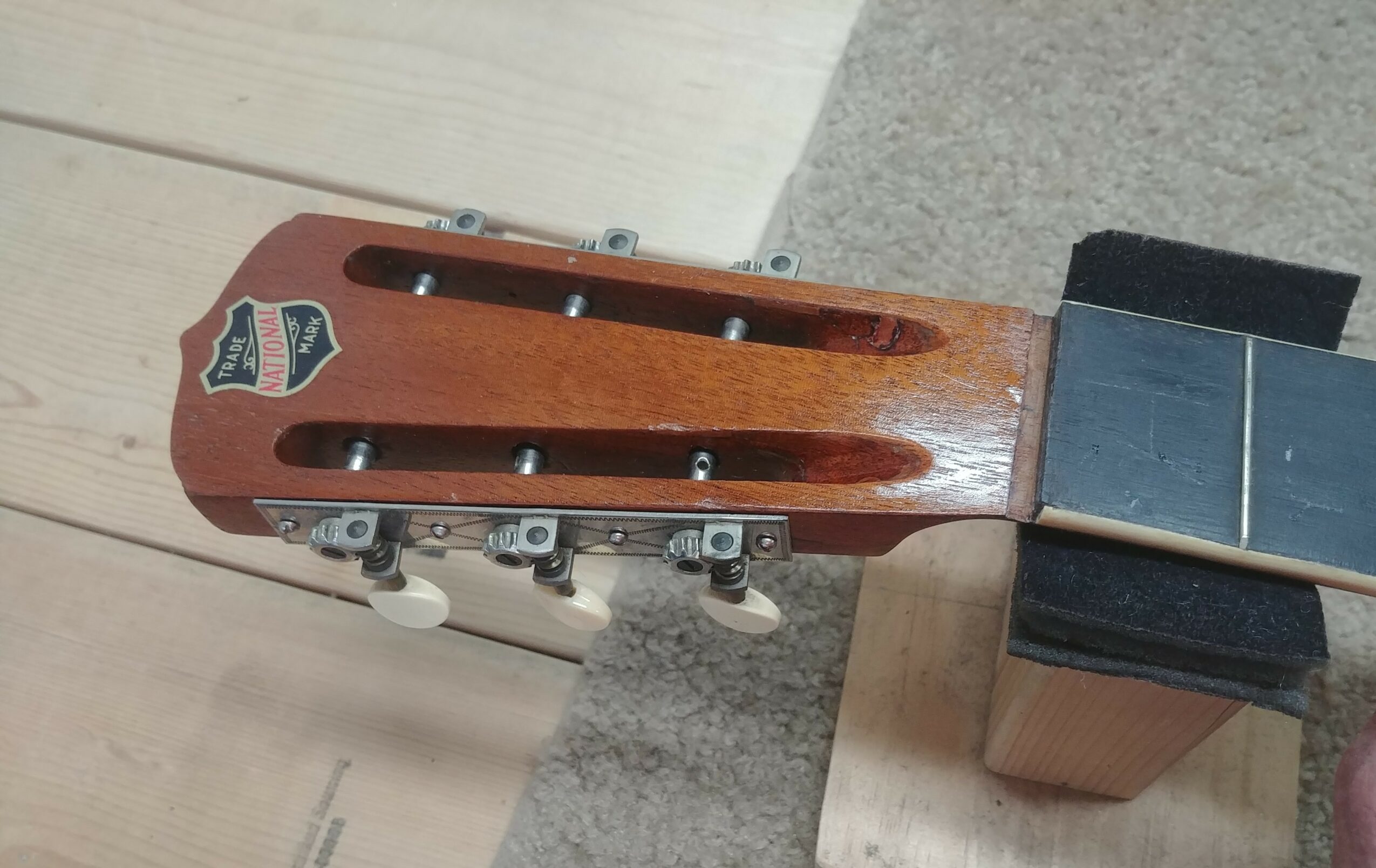 Headstock of a guitar with tuning pegs and a logo, resting on a stand.