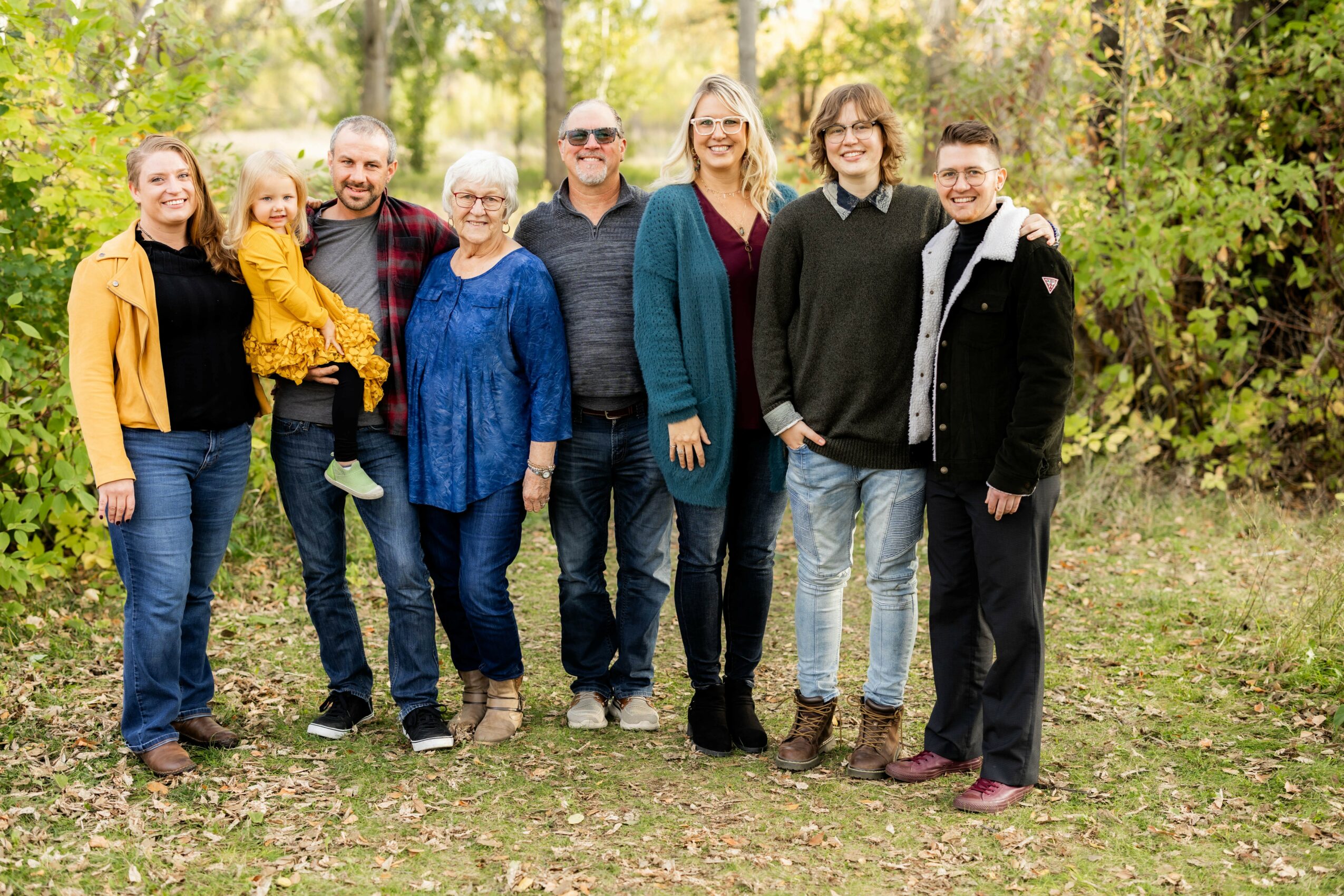 Group of nine people standing outdoors in a park with trees and grass, smiling at the camera.