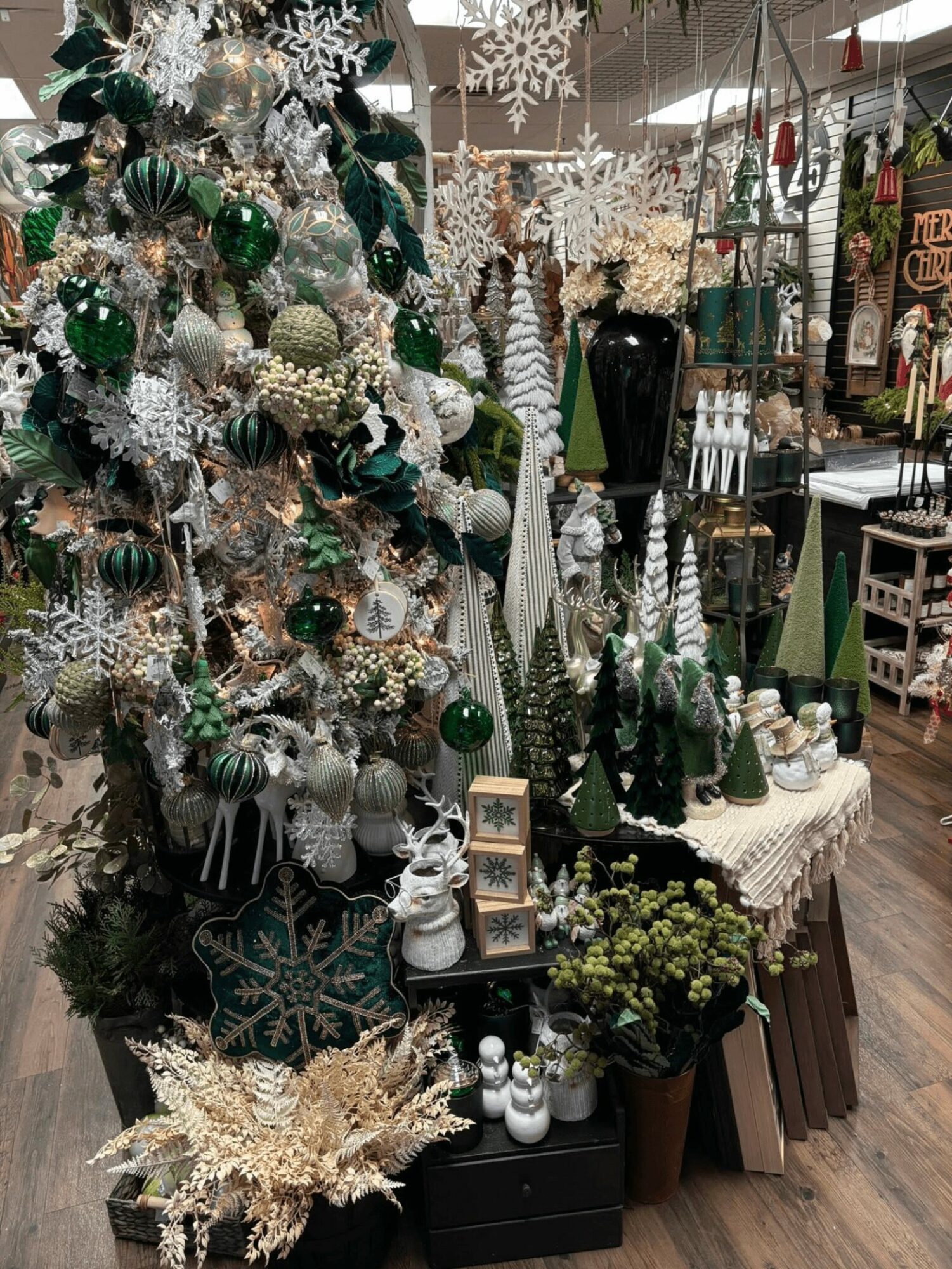 Decorative Christmas display with white, green, and silver ornaments, snowflakes, and festive decorations on tables and a tree.