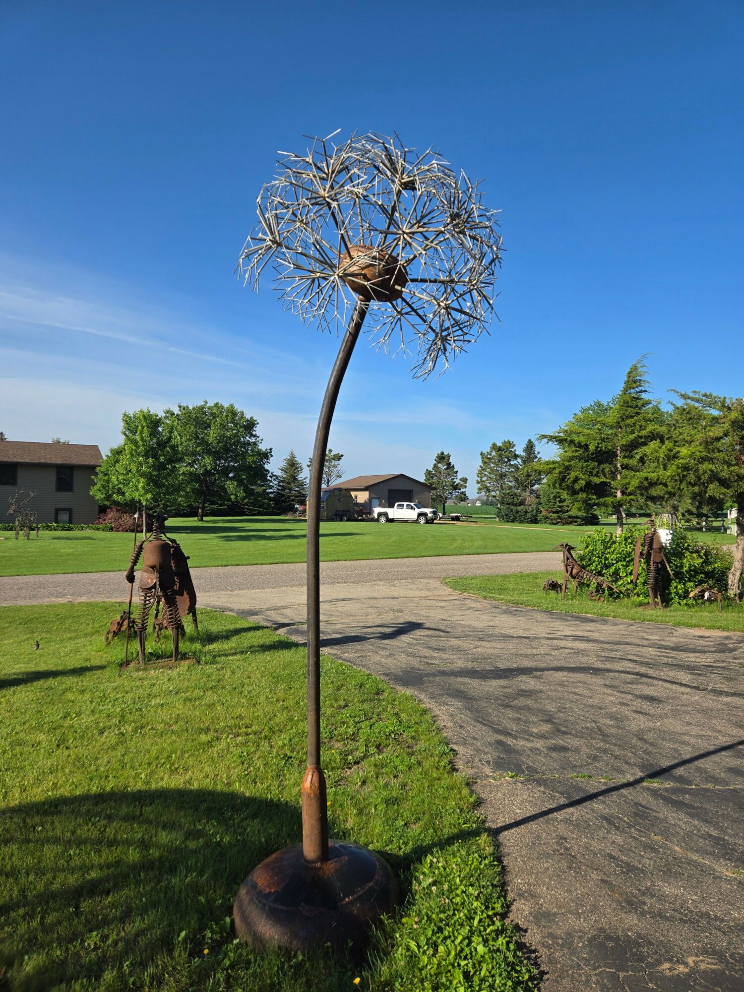 Tree with sparse branches and a person walking on a sidewalk, with a grassy area and buildings in the background.