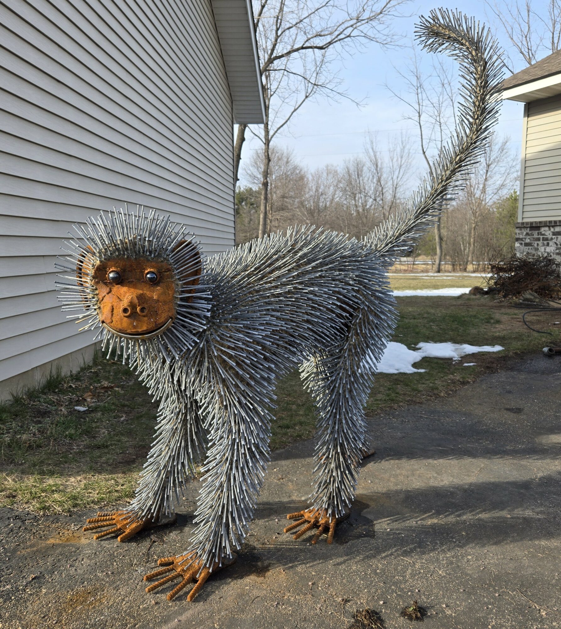 A sculpture of a creature with a lion's face and a body covered in metallic, spiky fur, standing outdoors on pavement.