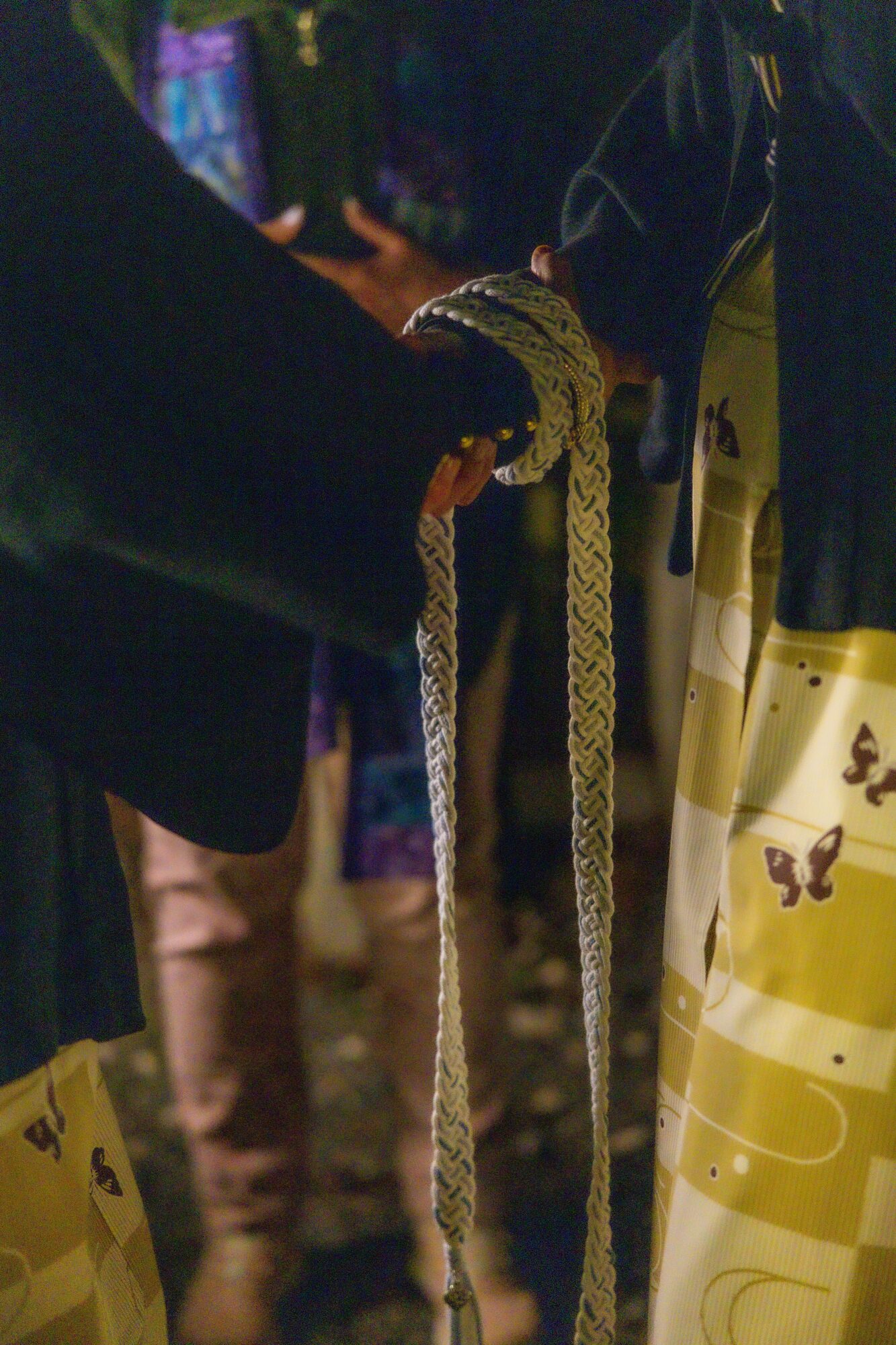 Person holding a rope with another person wearing a yellow and black outfit nearby, in a dimly lit environment.