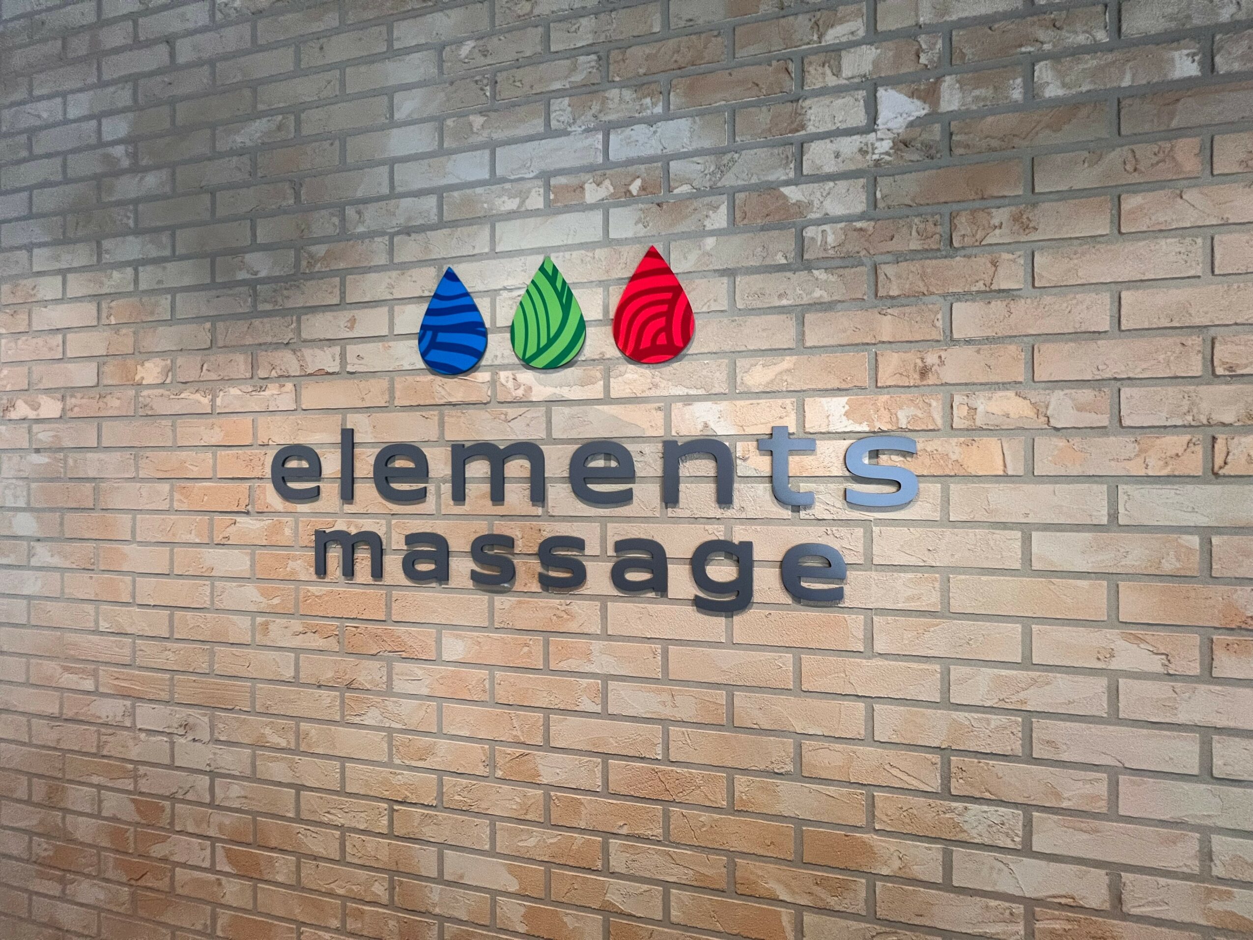 Brick wall with a sign reading 'elements massage' and three colorful water droplet icons above.
