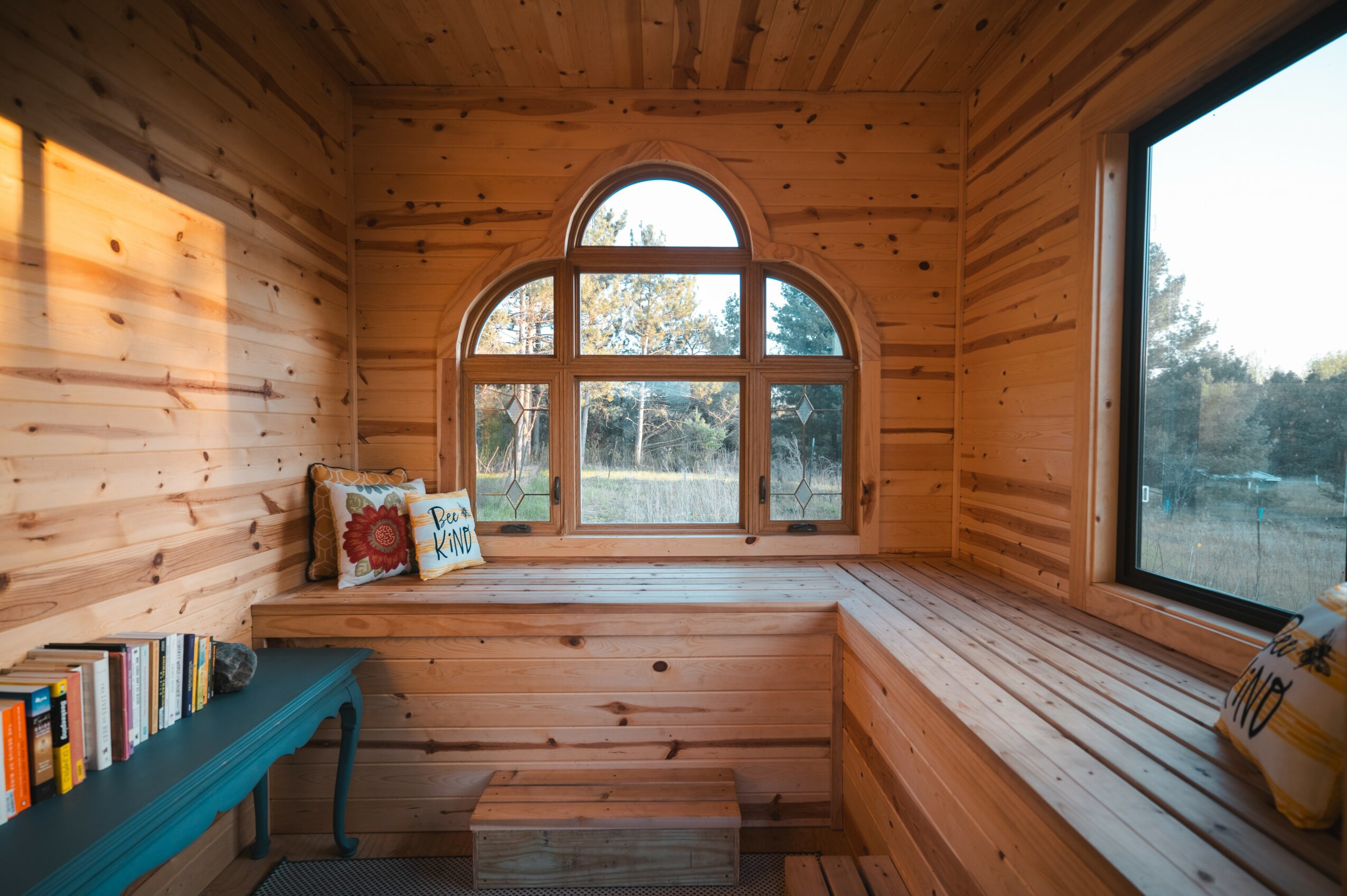 Wood-paneled interior with a large arched window, a bench with pillows, and a window seat with books.