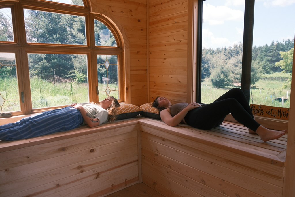 Two children lying on a wooden window seat, looking outside at a landscape with trees and sky.