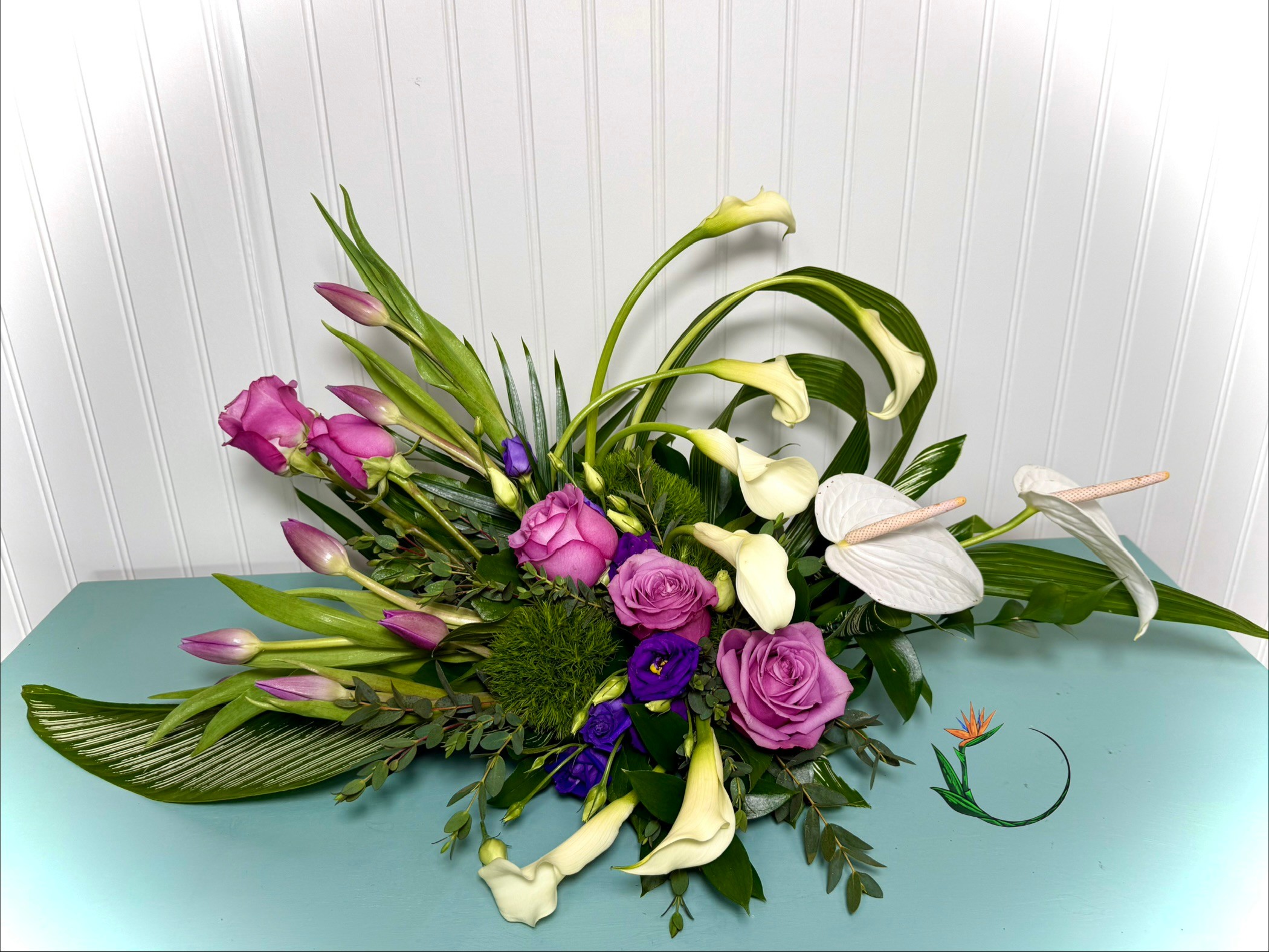 Arrangement of pink, purple, and white flowers with green leaves on a light blue surface, against a white paneled background.