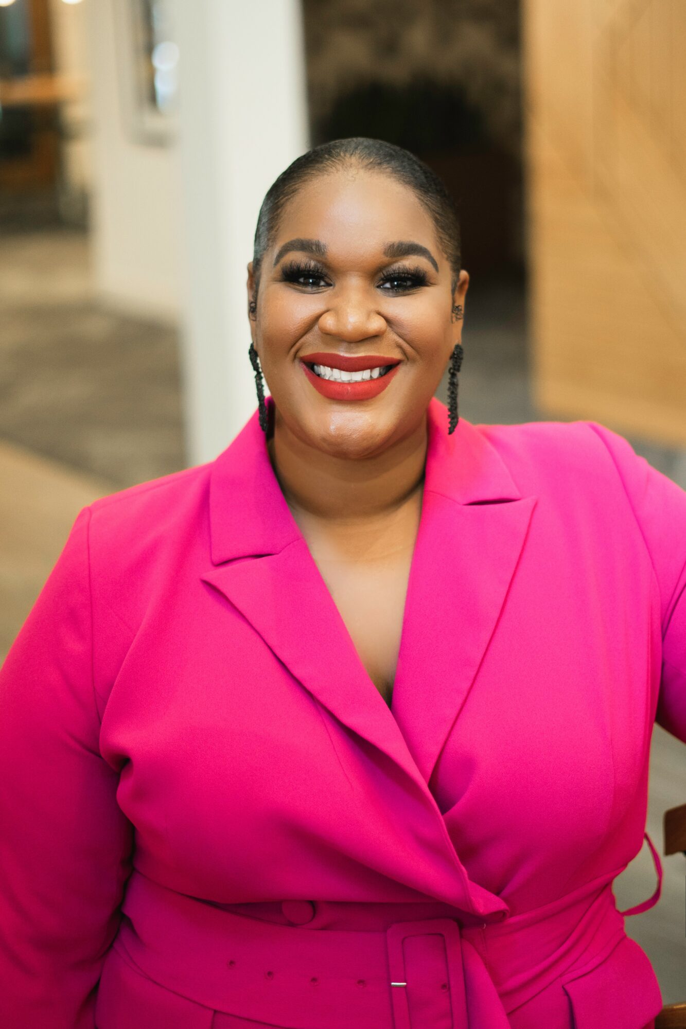 Smiling woman with dark hair in a bun, wearing a bright pink blazer, standing outdoors at night.