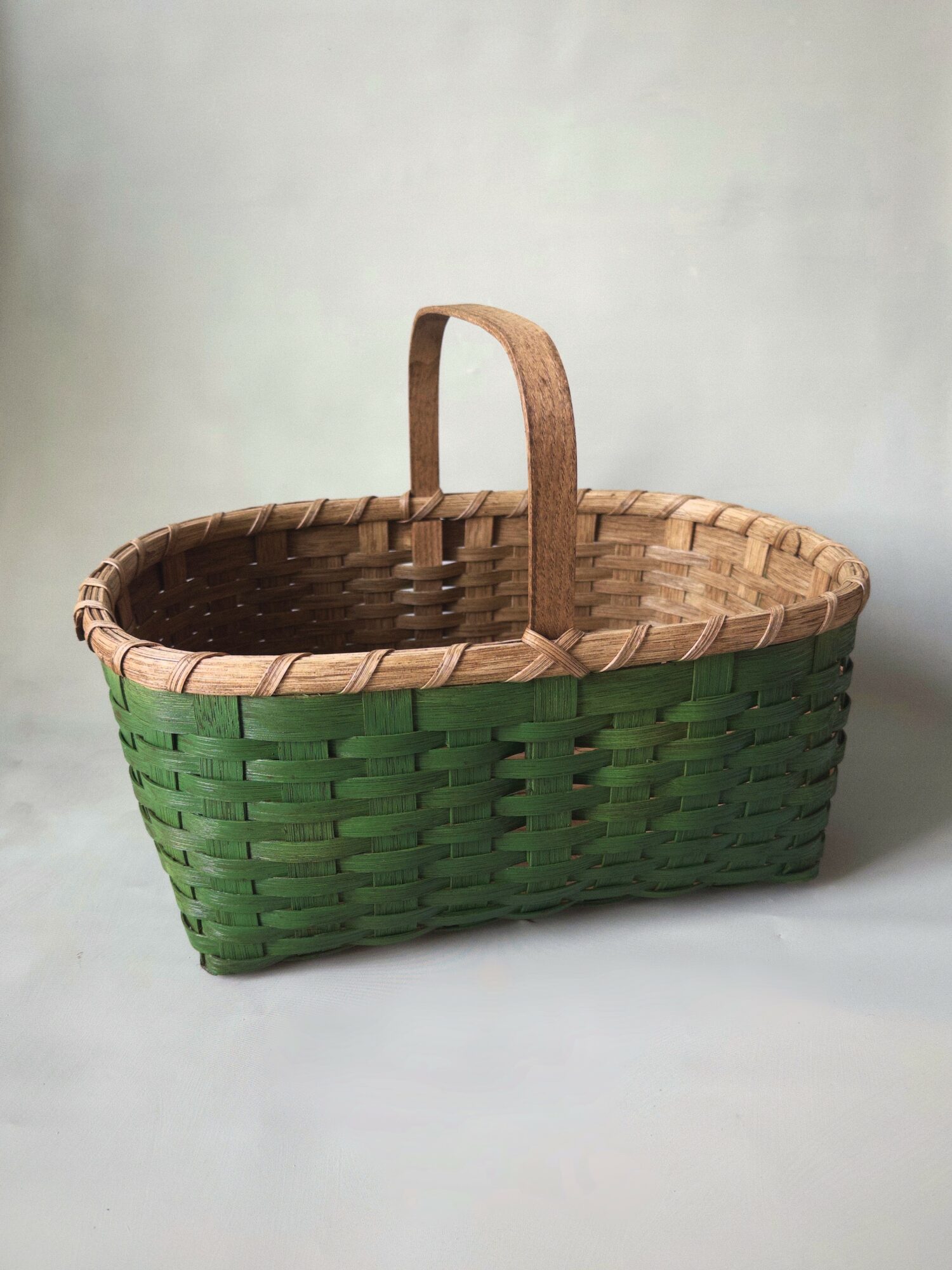 Woven basket with a handle, partially painted green, on a plain background.