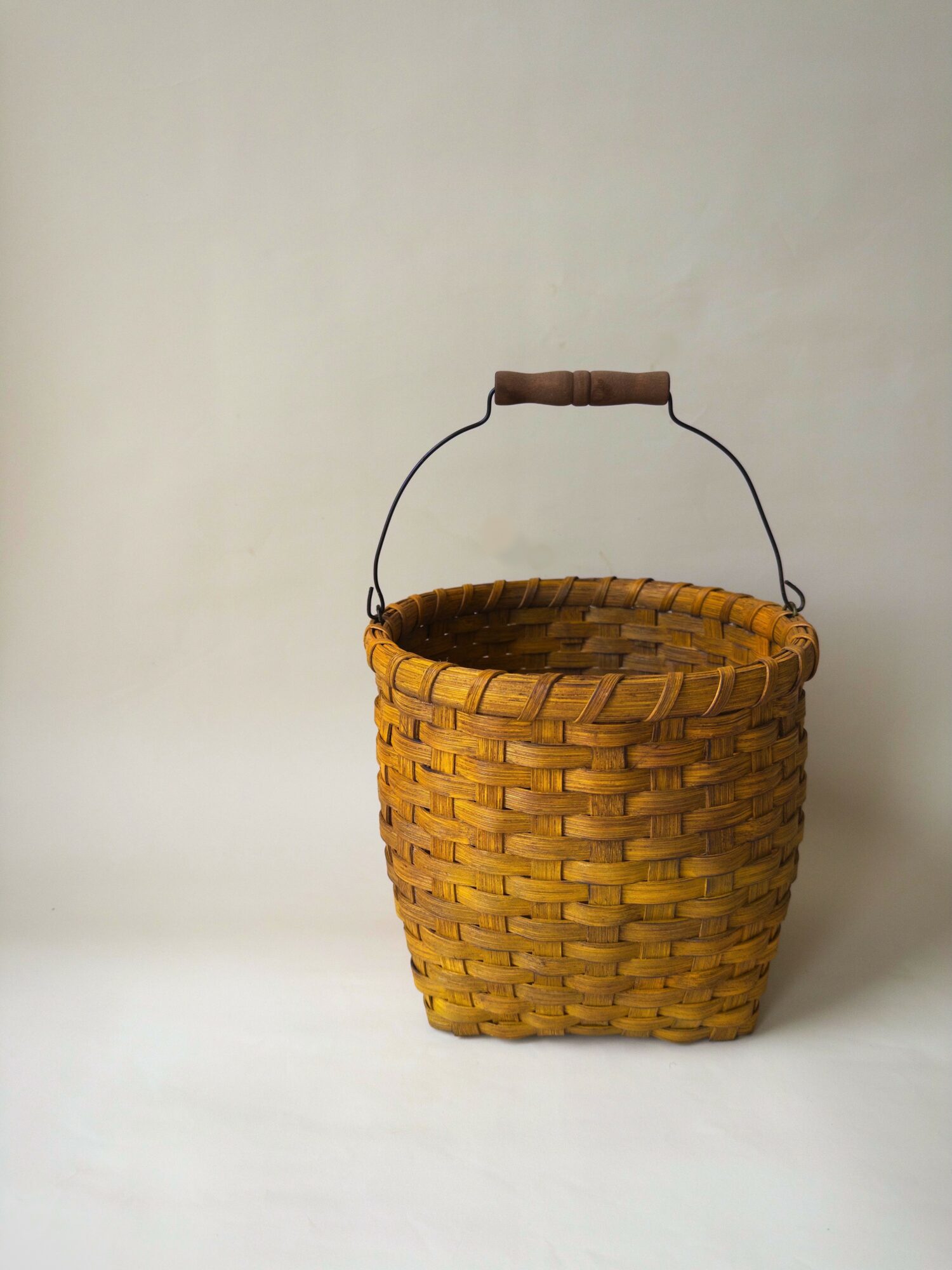 Woven basket with a handle, placed against a plain background.