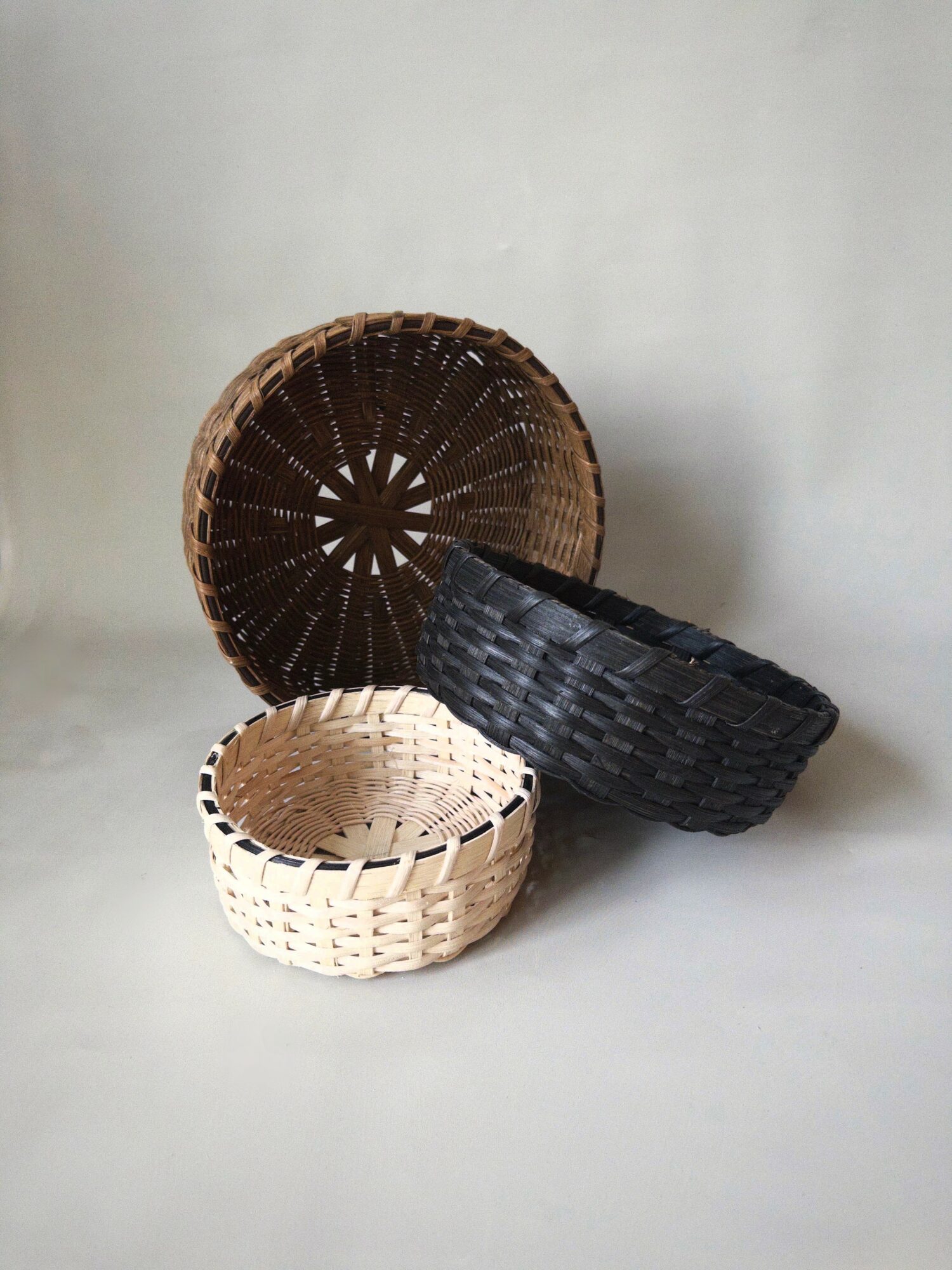 Four woven baskets of different sizes and colors stacked together against a plain background.