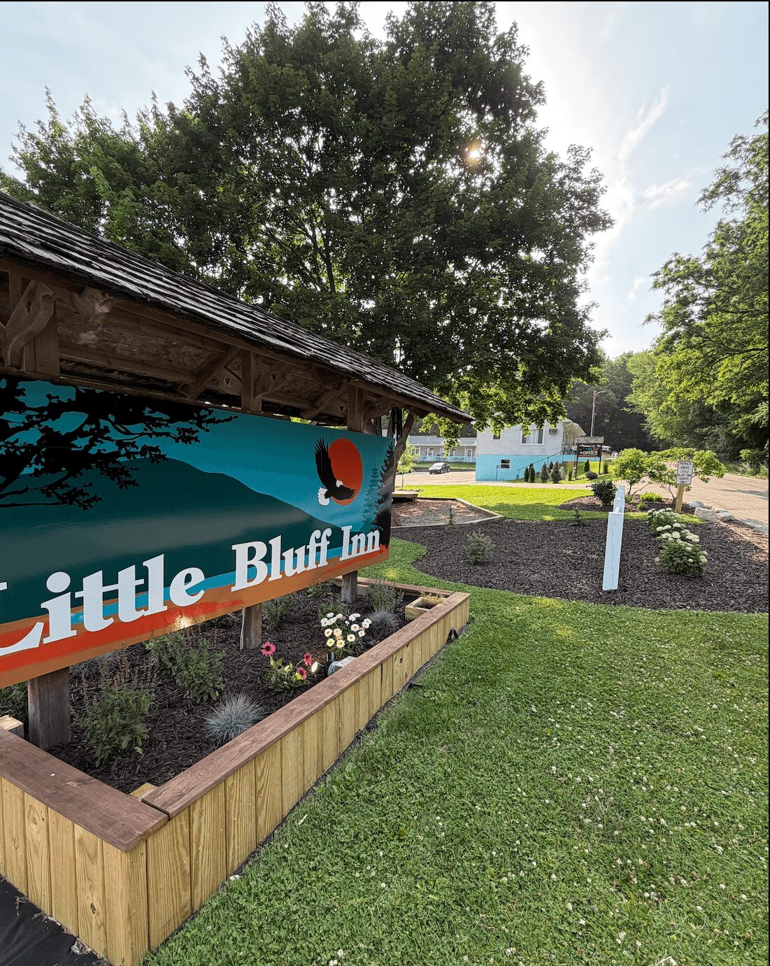 Outdoor scene with a building, a garden bed, trees, and a clear sky.