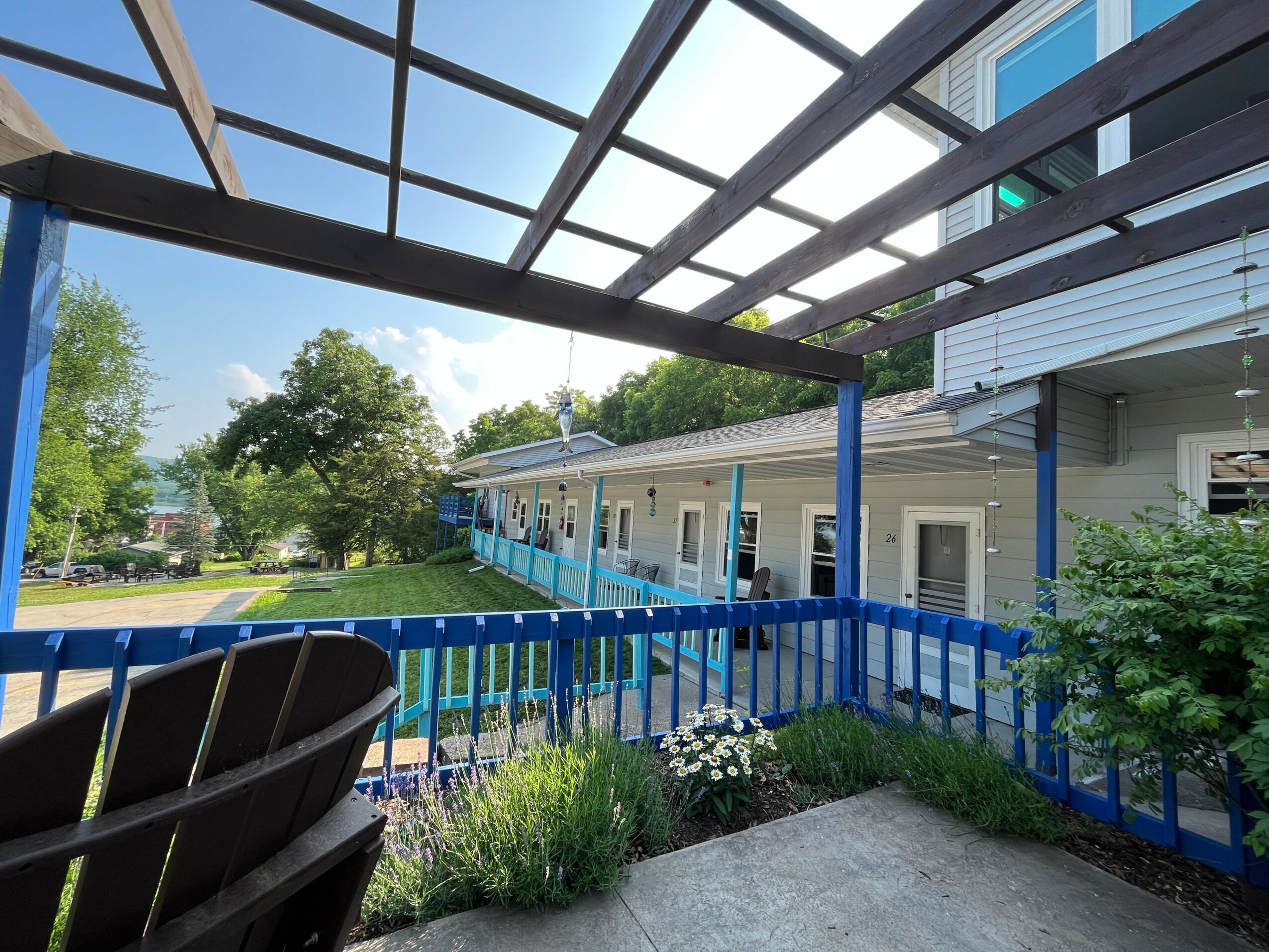 View from a covered patio looking at a building with a blue railing, trees, and a clear sky.