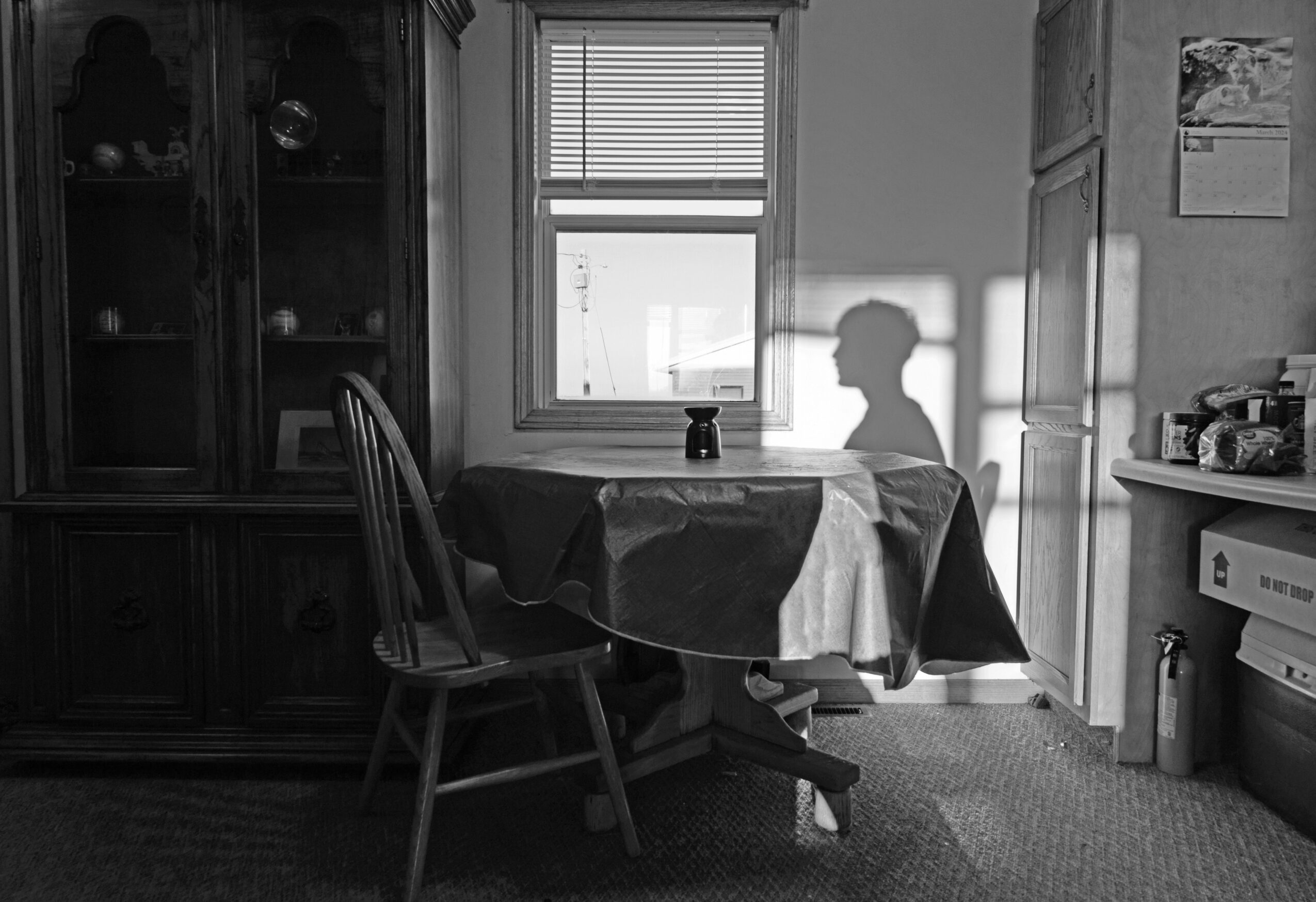Silhouette of a person sitting at a table with a window behind, casting a shadow on the wall, in a room with furniture.