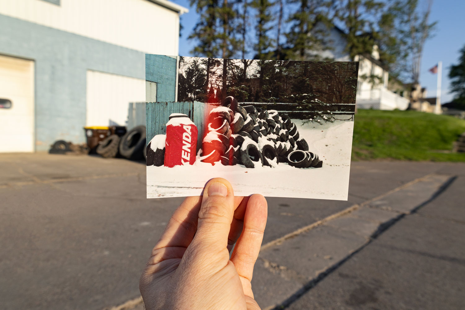 Person holding a photo of a pile of tires and a red and white object outdoors.