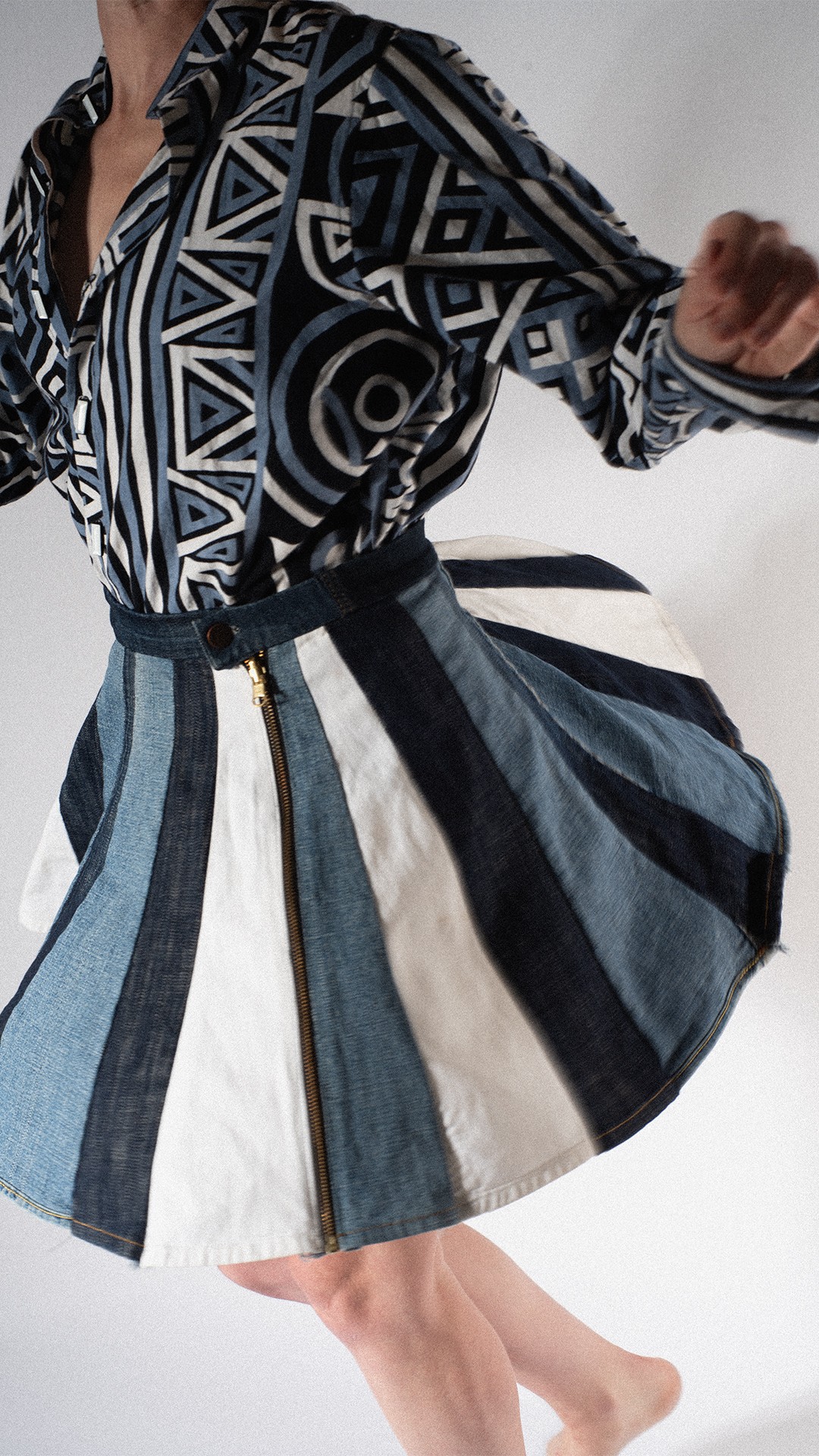 Person wearing a patterned top and a striped skirt, mid-movement, with one arm extended and legs visible.