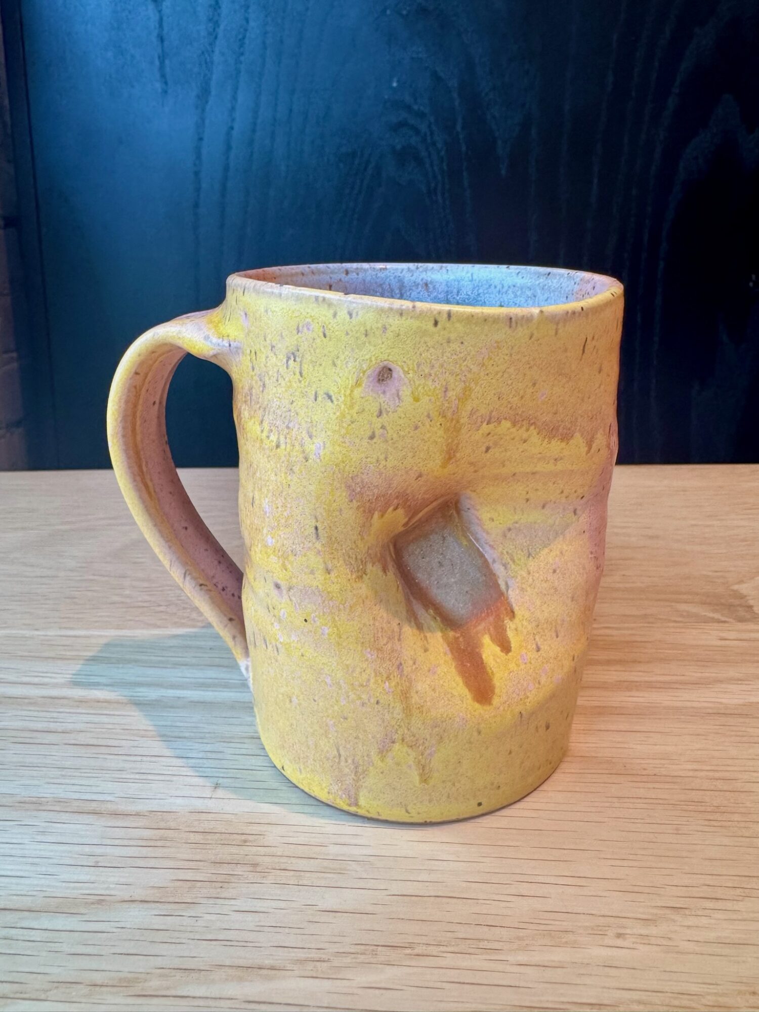 Yellow ceramic mug with a handle and a small protrusion on the side, placed on a wooden surface.