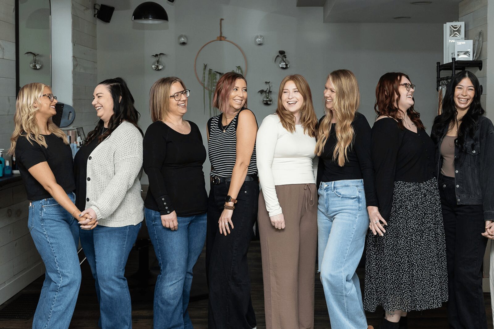 Group of eight women standing indoors, smiling and talking, with modern decor in the background.