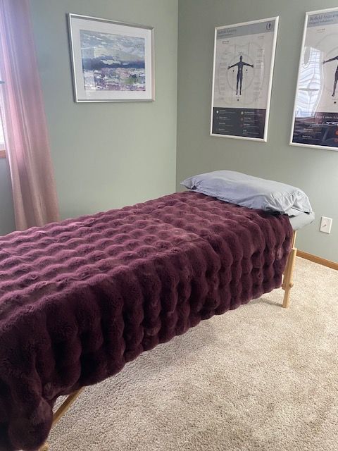 Bedroom with a bed covered in a purple textured blanket, light green walls, and framed pictures on the wall.