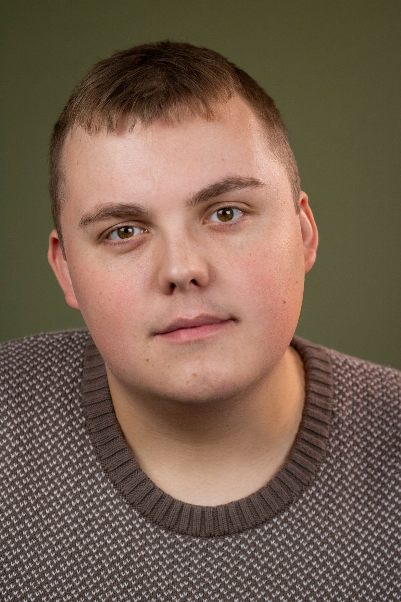 Young man with short brown hair and light skin, wearing a patterned sweater, against a green background.