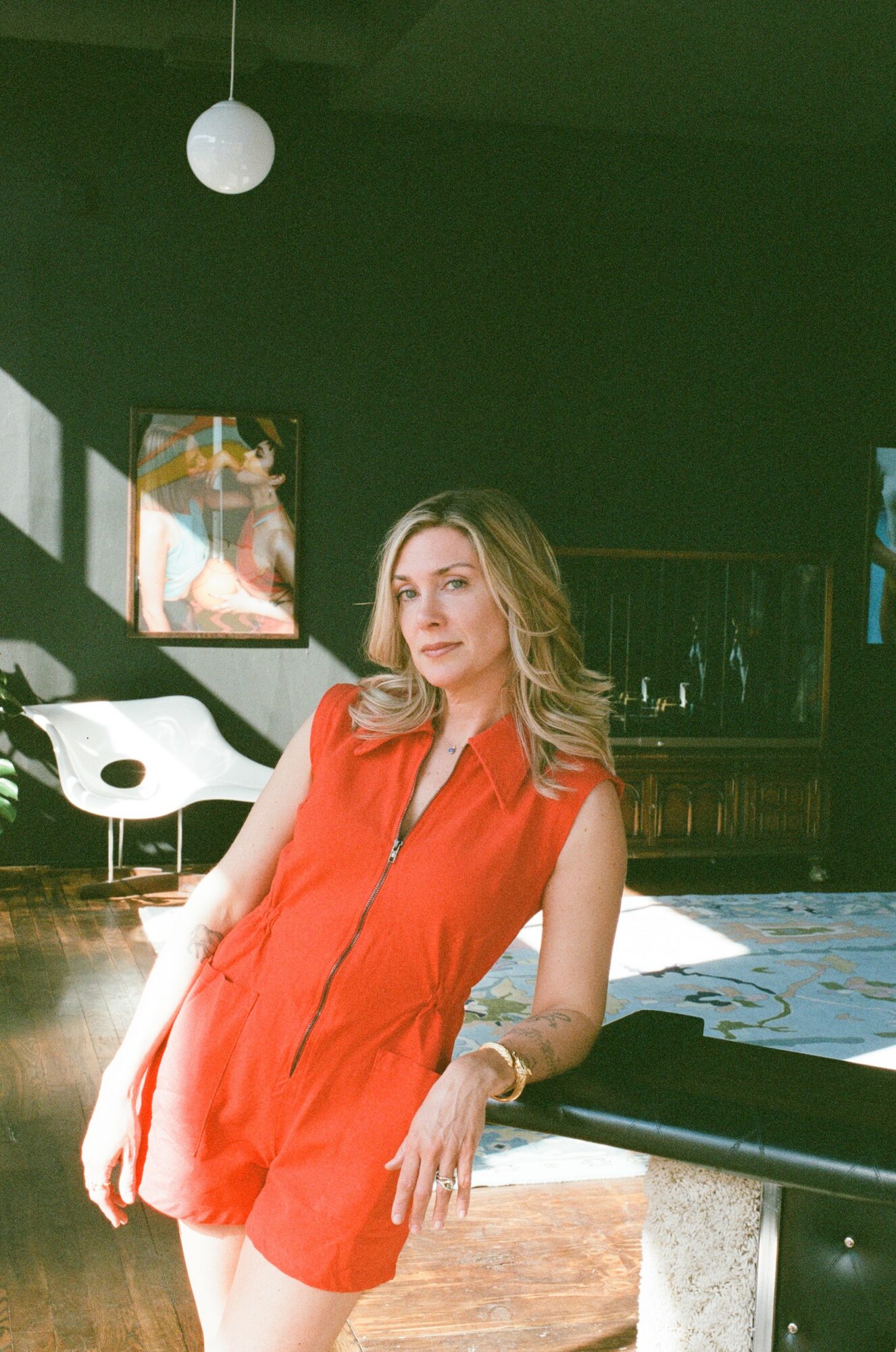 Woman in a red sleeveless outfit sitting at a table in a room with artwork and modern furniture.
