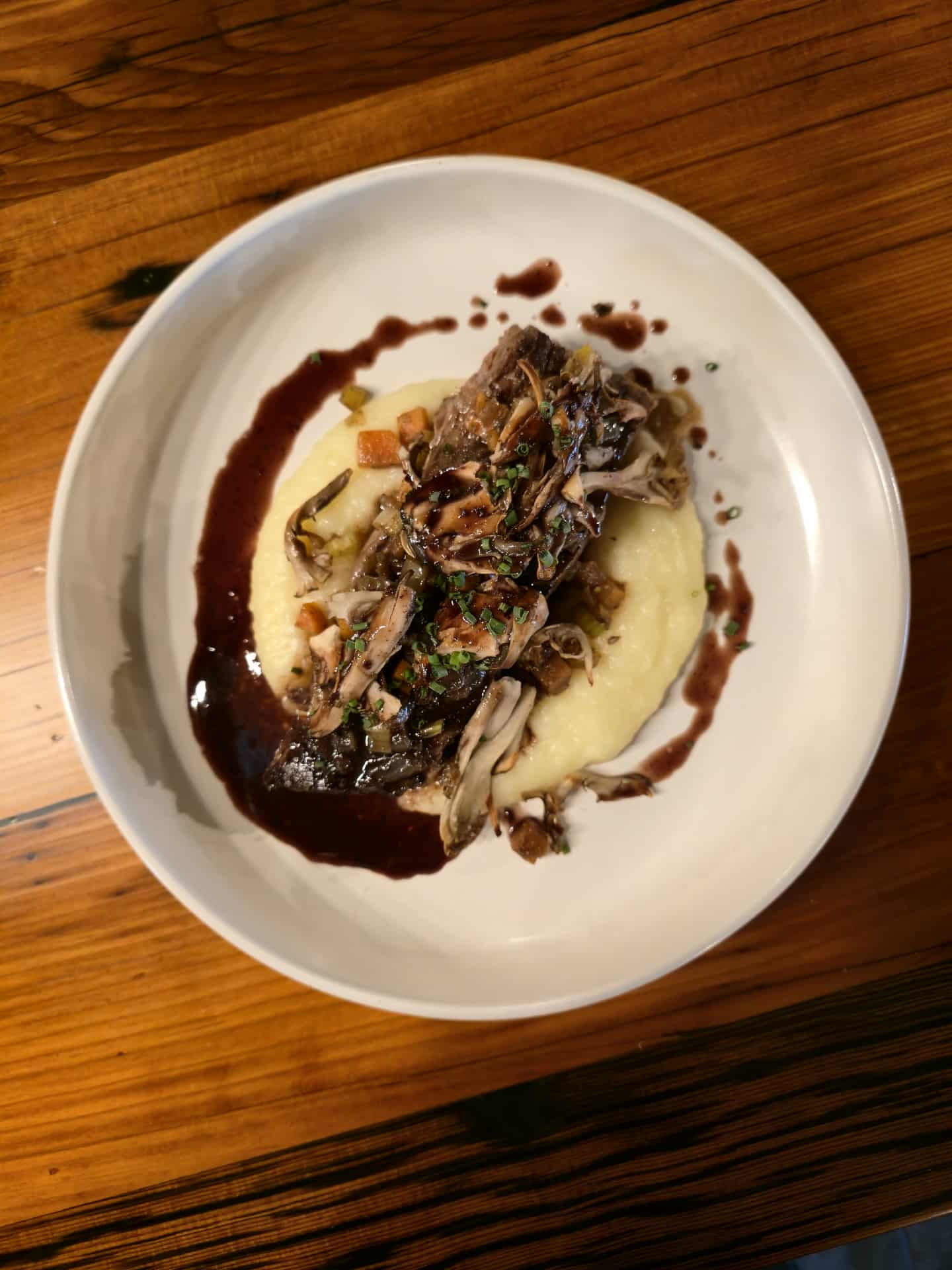 Plate with cooked fish, mashed potatoes, and sauce on a wooden table.