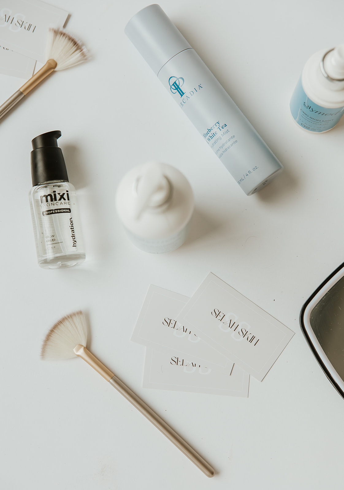 Skincare products, a brush, and paper on a white surface, with a mirror partially visible in the corner.