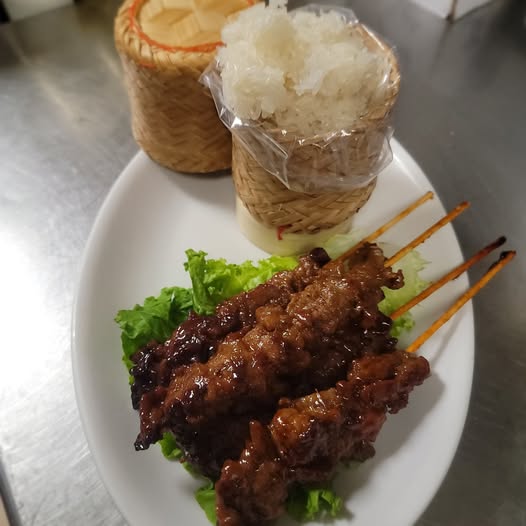 Skewered grilled meat served with lettuce, rice, and shredded coconut on a white plate.