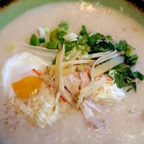 Bowl of creamy soup with poached eggs, chopped green onions, and herbs, garnished with shredded chicken and vegetables.