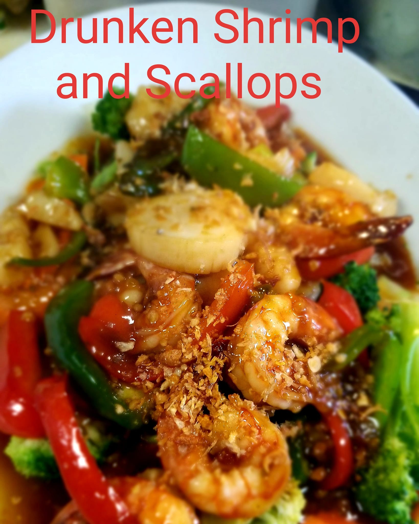 Close-up of a dish with shrimp, scallops, and vegetables in sauce, garnished with crumbs, in a white bowl.